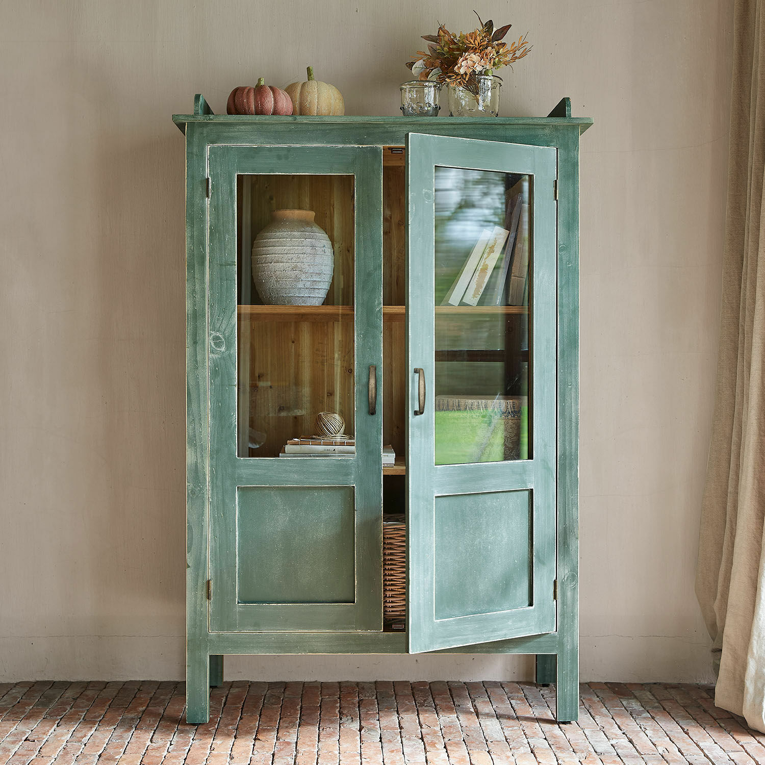 Groene houten kast met glazen deuren en decoraties bovenop, rustiek woonkamermeubel