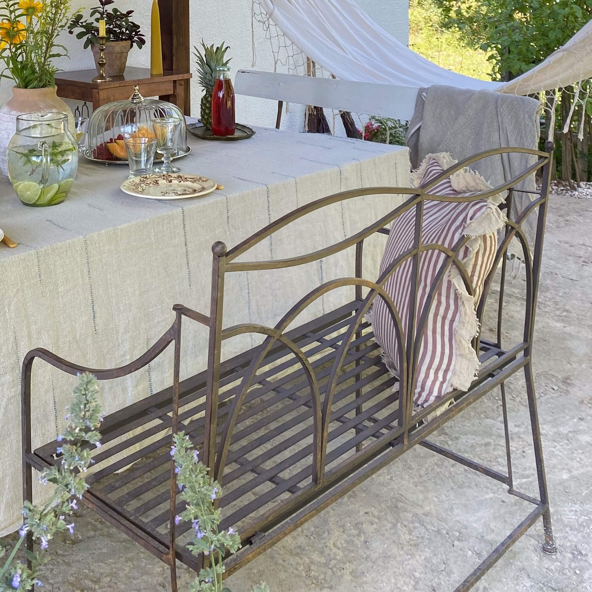 Metalen tuinbank in vintage stijl met gestreept kussen naast gedekte tafel buiten