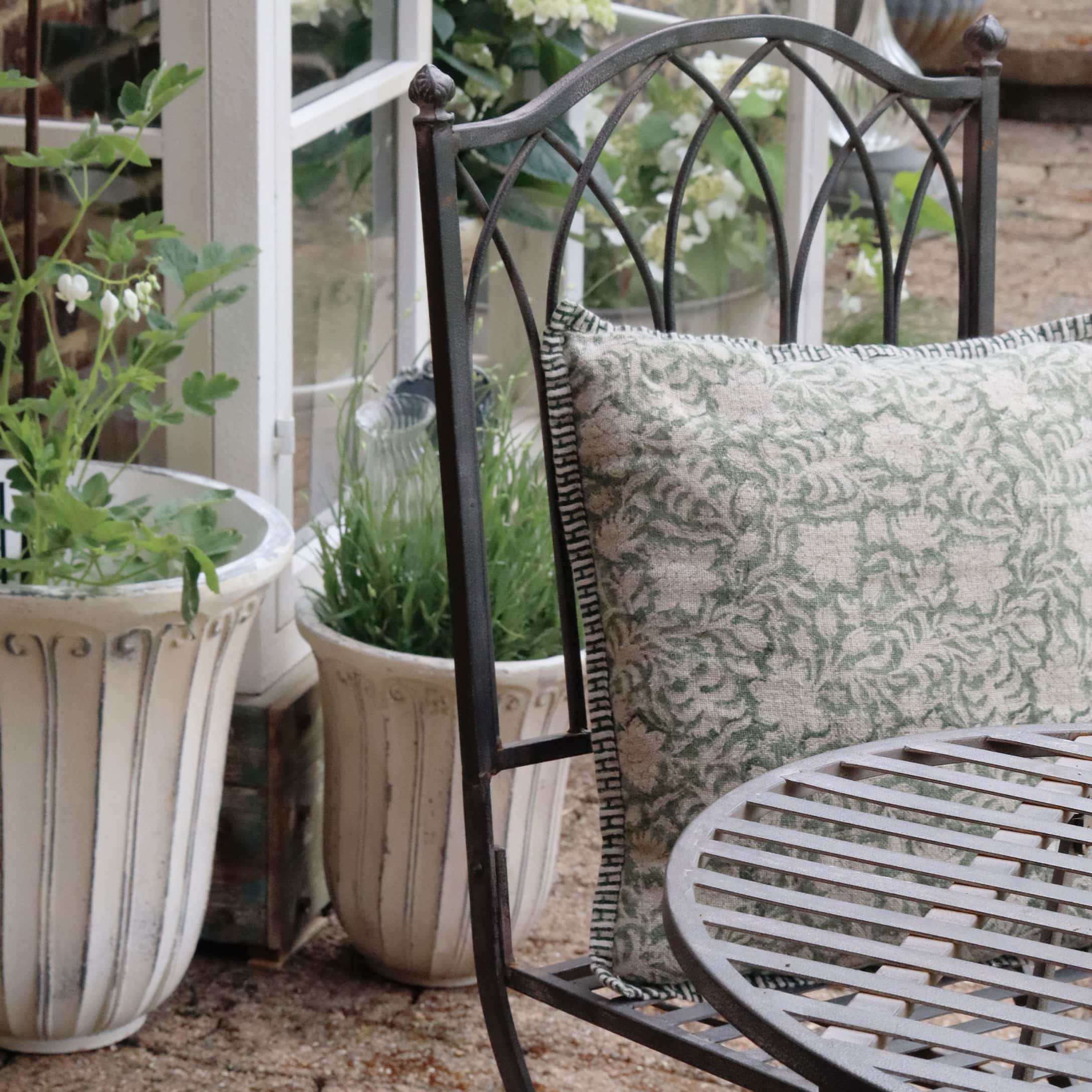 Metalen tuinstoel met groen-beige kussen en decoratieve plantenpotten op de achtergrond
