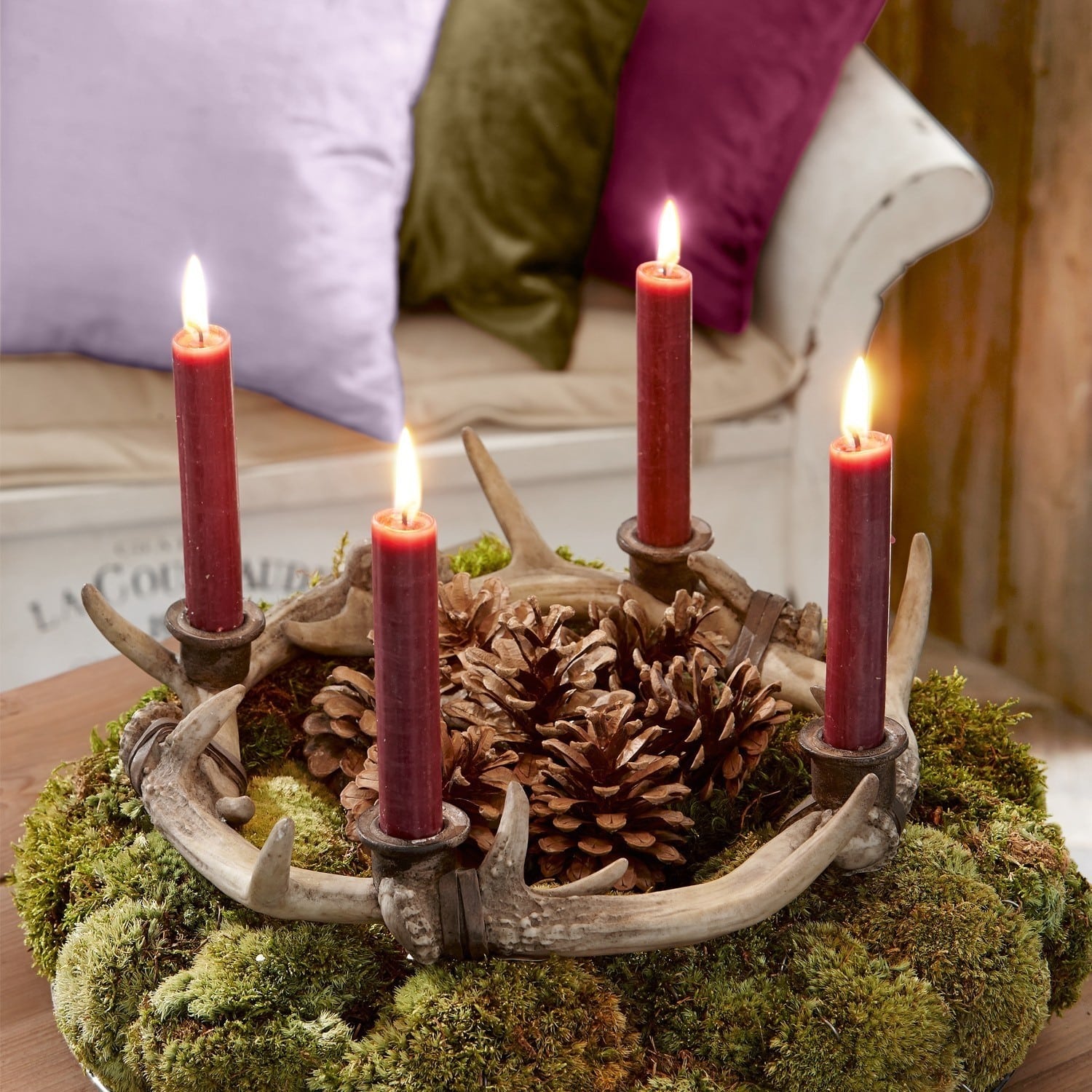 Kaarshouder van gewei met rode kaarsen en dennenappels op groen mos voor interieurdecoratie
