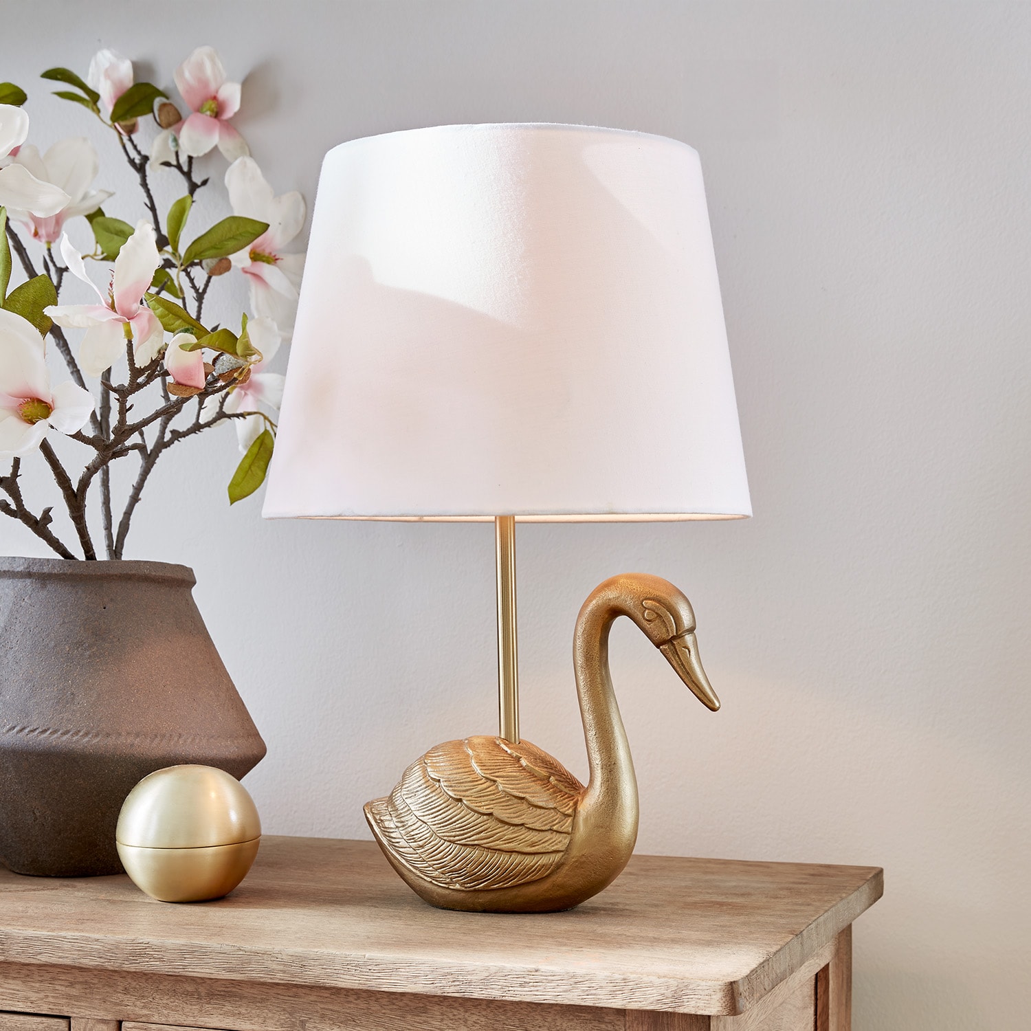 Gouden tafellamp in zwaanvorm met witte kap op houten tafel met bloemdecoratie
