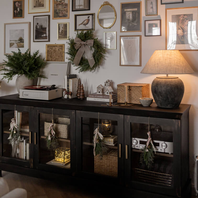 Zwarte houten dressoir met glazen deuren, kerstdecoraties en keramische lamp in gezellige woonkamer