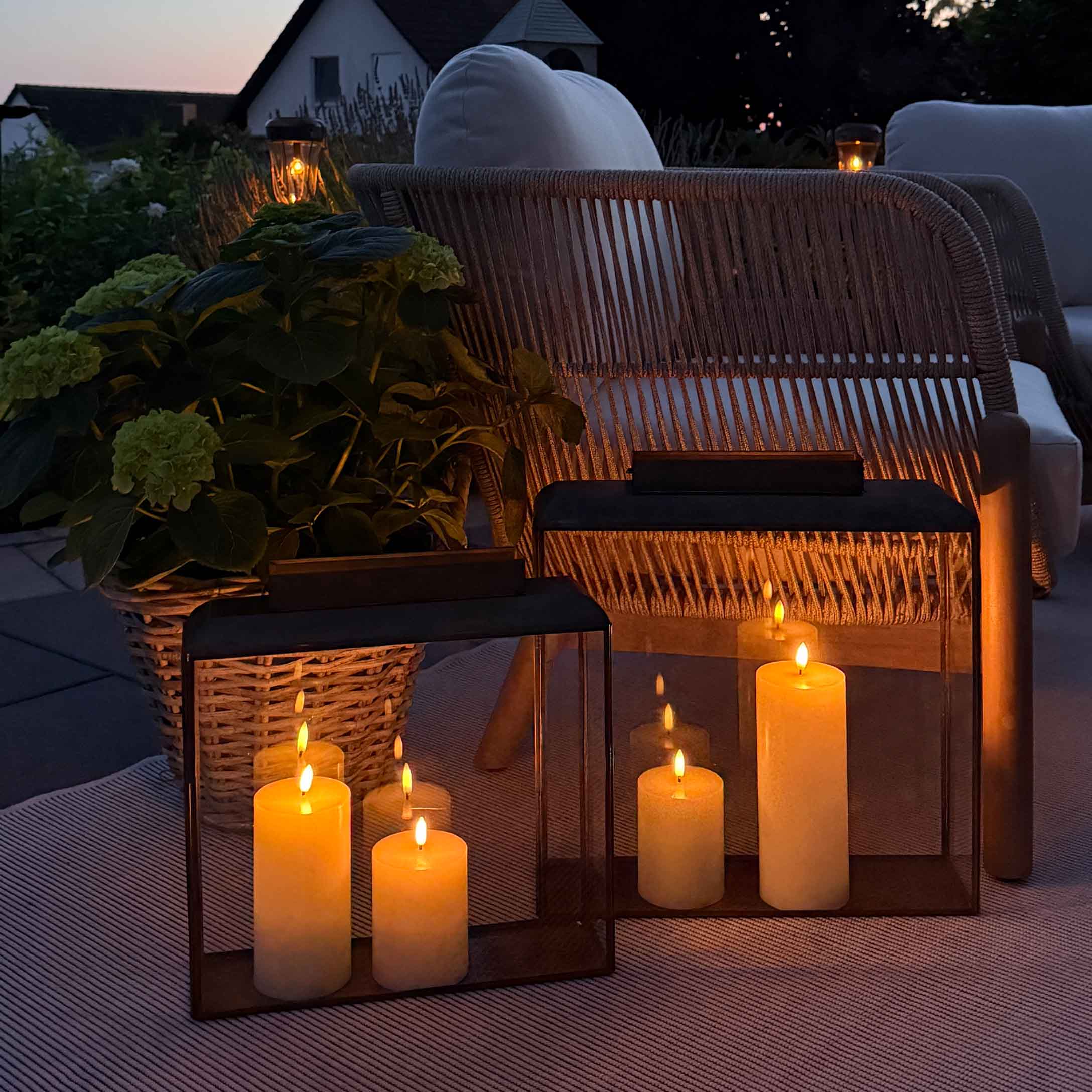 Sfeerverlichting met lantaarns en kaarsen op terras met rotan stoel en wit kussen