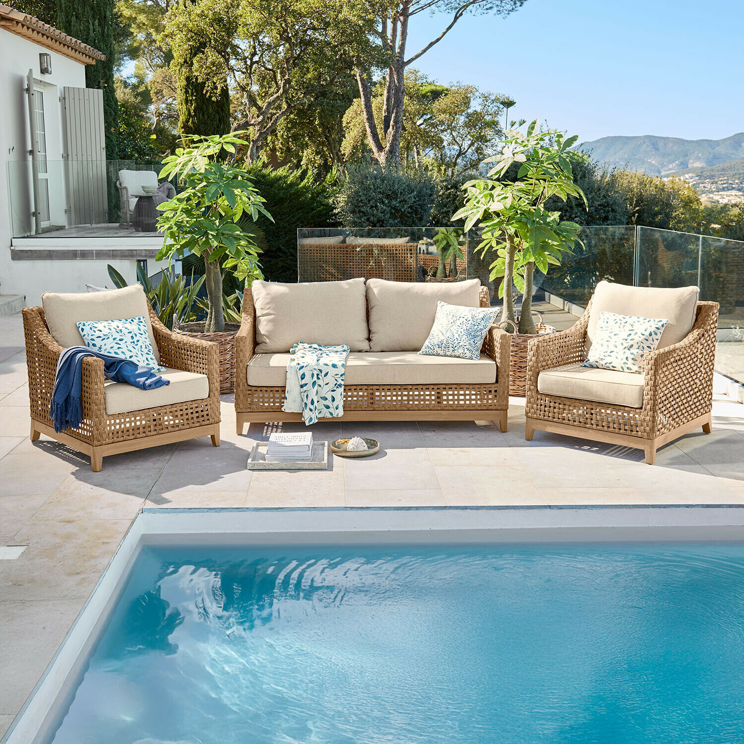 Tuinmeubelset van bruin rattan met beige kussens bij een zwembad buiten