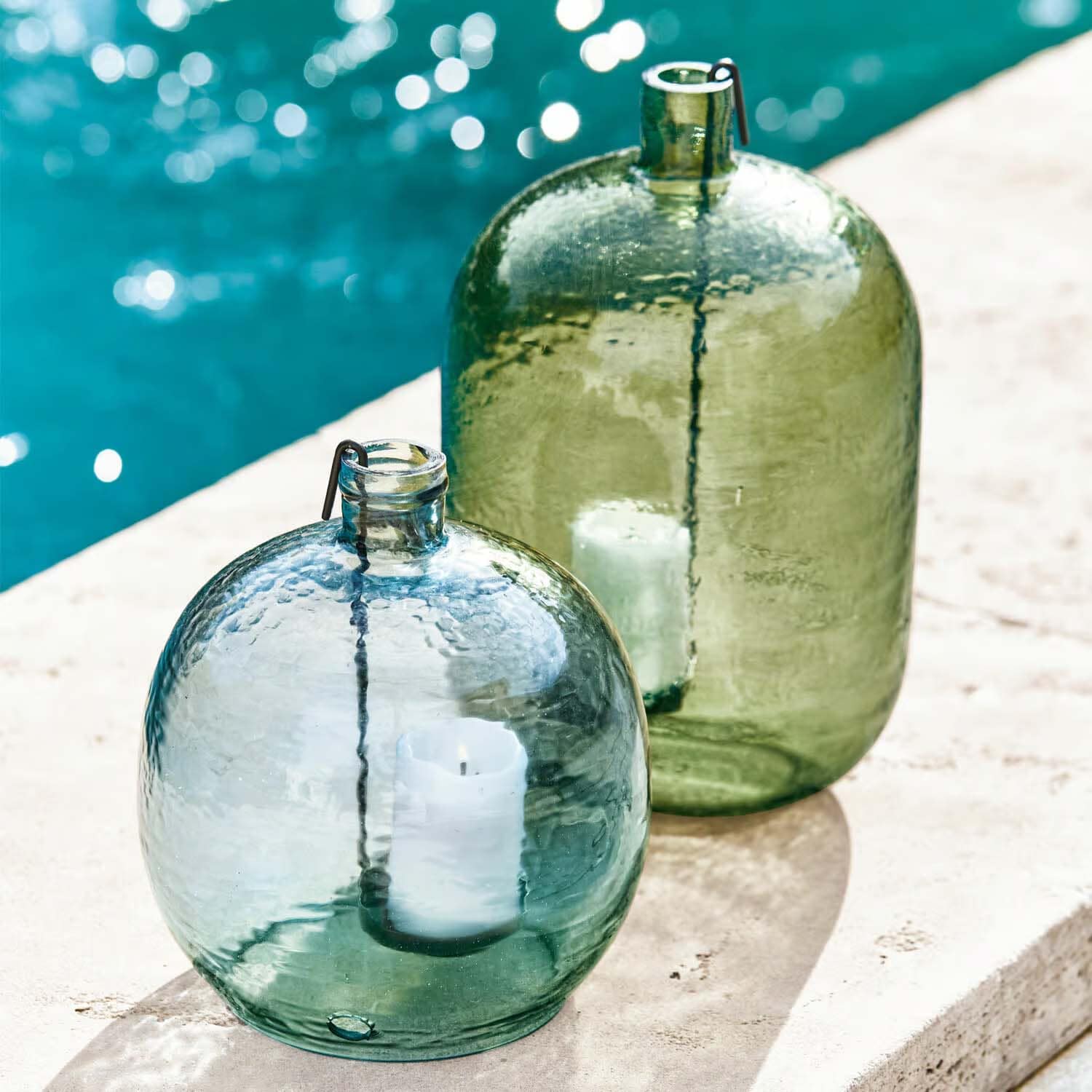 Glazen lantaarns in groen en blauw met witte kaarsen, buitendecoratie bij het zwembad