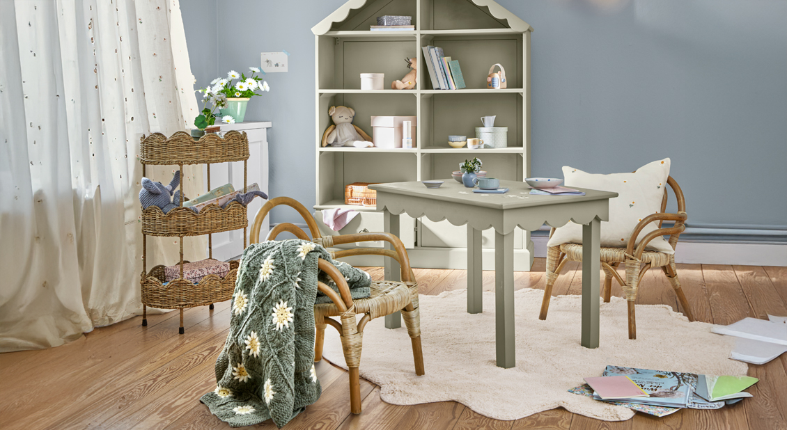 Zachtblauwe kinderkamer met houten tafel en rotan stoelen op lichte vloerkleed