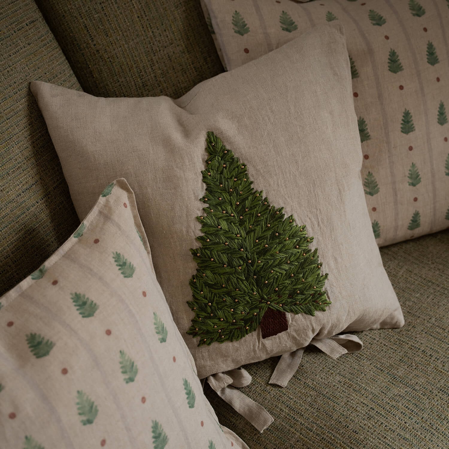 Beige linnen kussen met groen geborduurde boom en gouden kralen op een bank