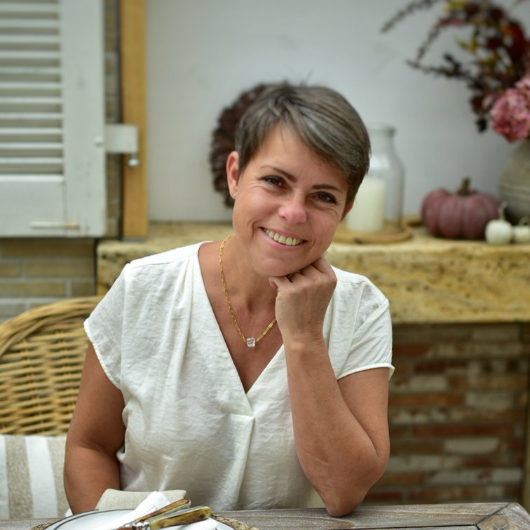Lachende vrouw in wit shirt zittend aan tafel met herfstdecoratie op de achtergrond