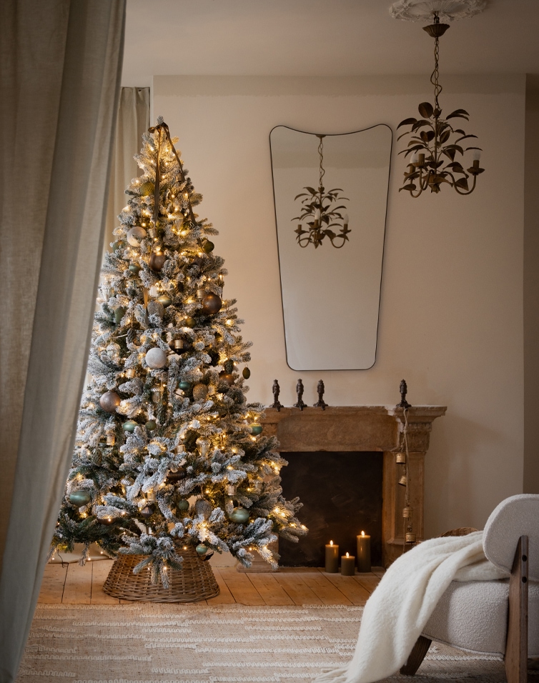 Besneeuwde kerstboom met warme verlichting en versiering in gezellige woonkamer met open haard