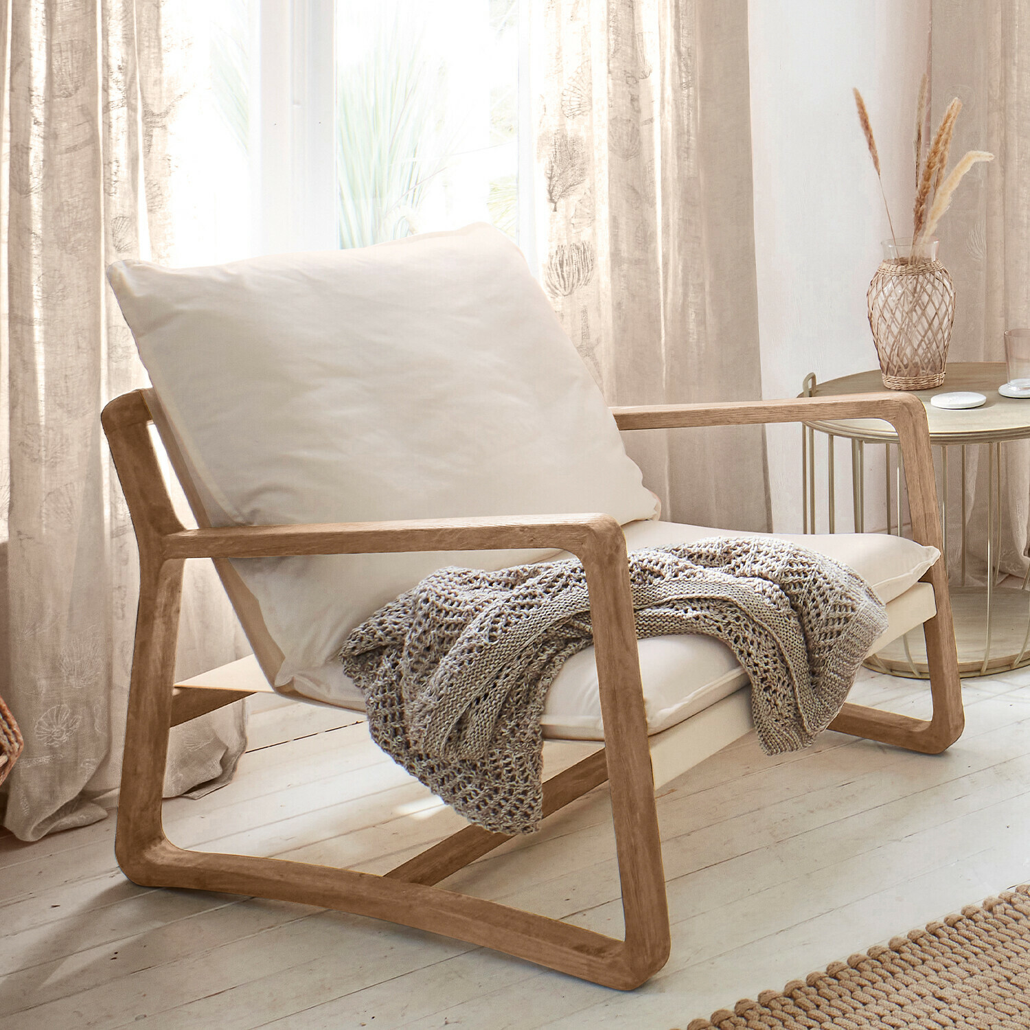 Fauteuil Jowna Stoel van licht hout met crèmekleurig kussen en grijze gebreide deken in lichte woonkamer