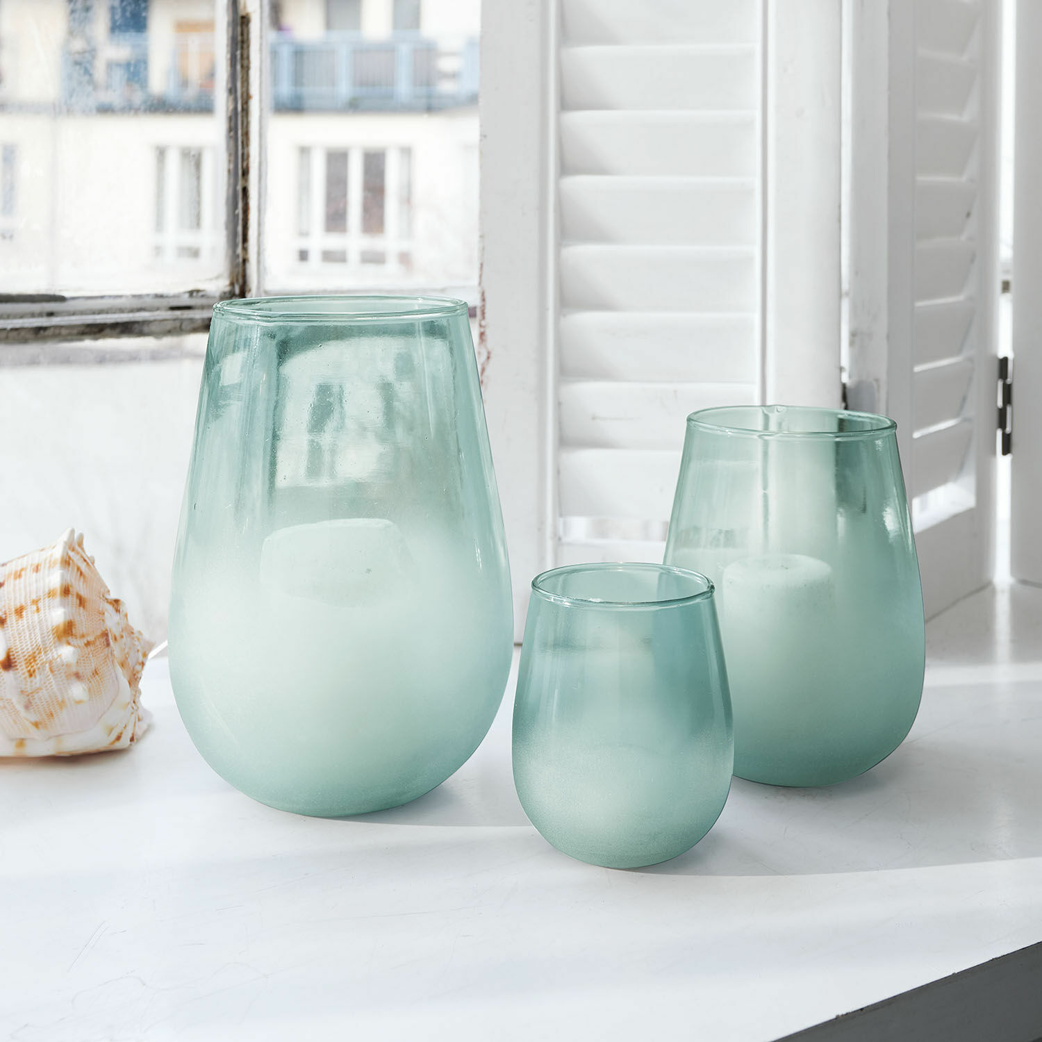 Windlicht set van 3 Miristelle Set van drie matte groene glazen windlichten op een witte vensterbank met witte kaarsen