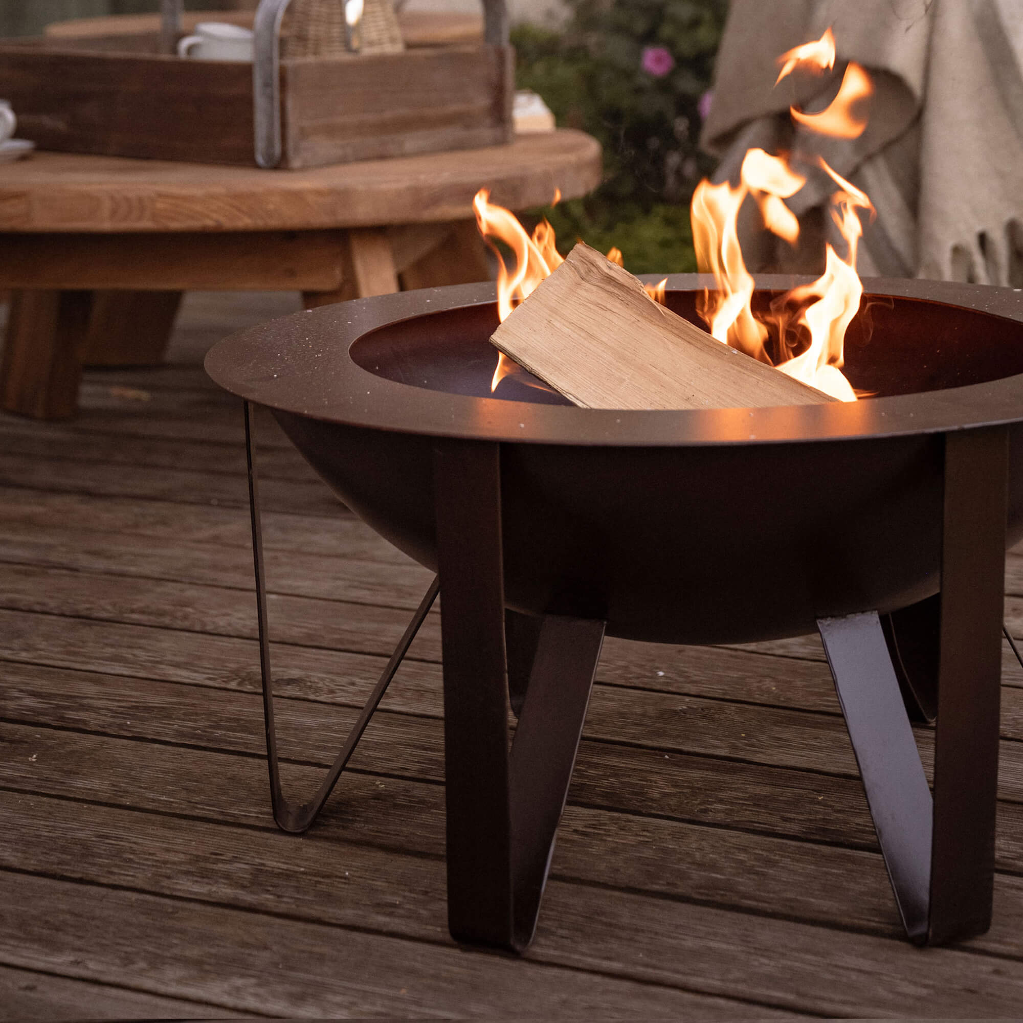 Zwarte metalen vuurkorf met brandend hout op houten terras, perfect voor tuin en ontspanning