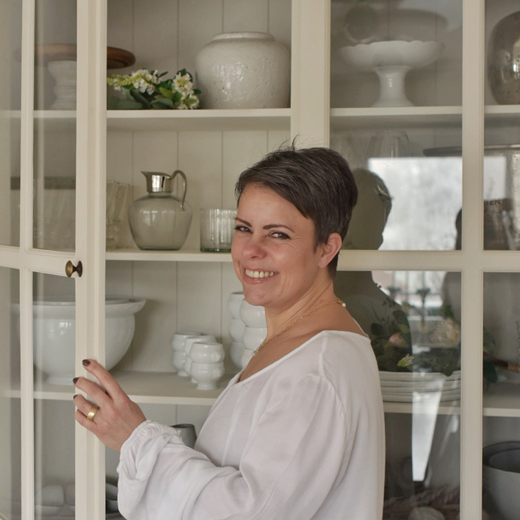Vrouw in witte blouse opent crèmekleurige kast met porselein en decoraties thuis