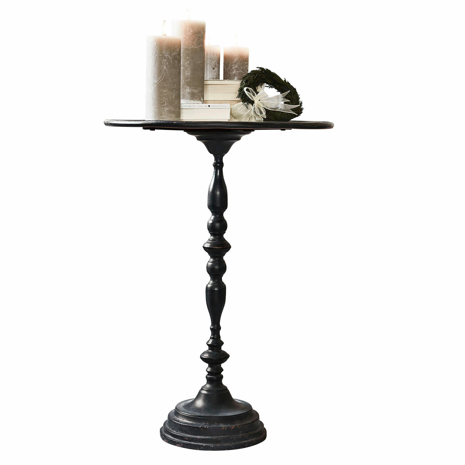 Zwarte metalen bijzettafel met ronde blad en decoratieve voet, versierd met kaarsen en krans