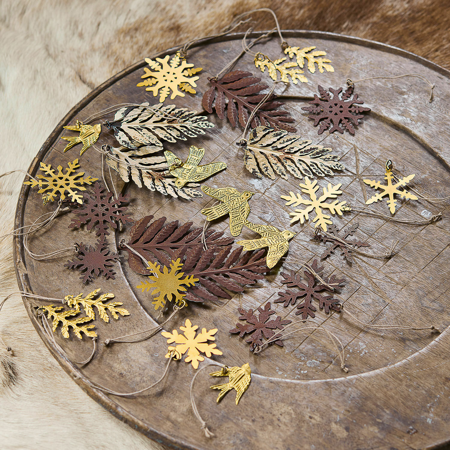 Metalen decoraties in de vorm van bladeren, vogels en sneeuwvlokken in goud en bruin op een houten schaal