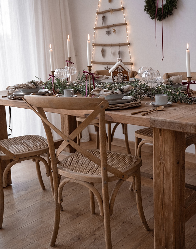 Houten tafel met natuurlijke stoelen en kerstdecoratie met peperkoekhuisje en kaarsen
