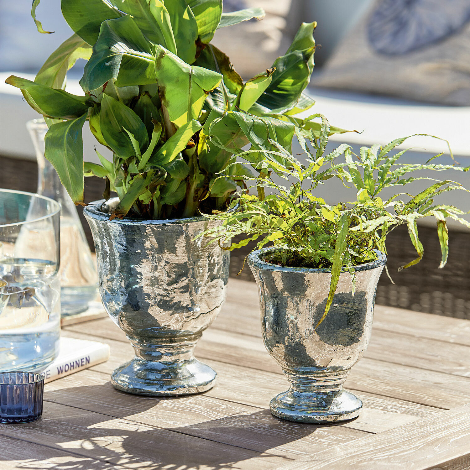 Twee zilverkleurige metalen plantenbakken met groene planten op houten tafel in lichte omgeving