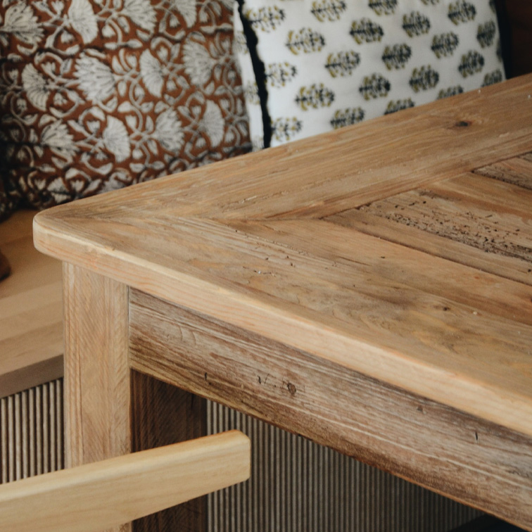 Tafel van licht hout met rustieke uitstraling en decoratieve kussens op de achtergrond, woonkamermeubilair