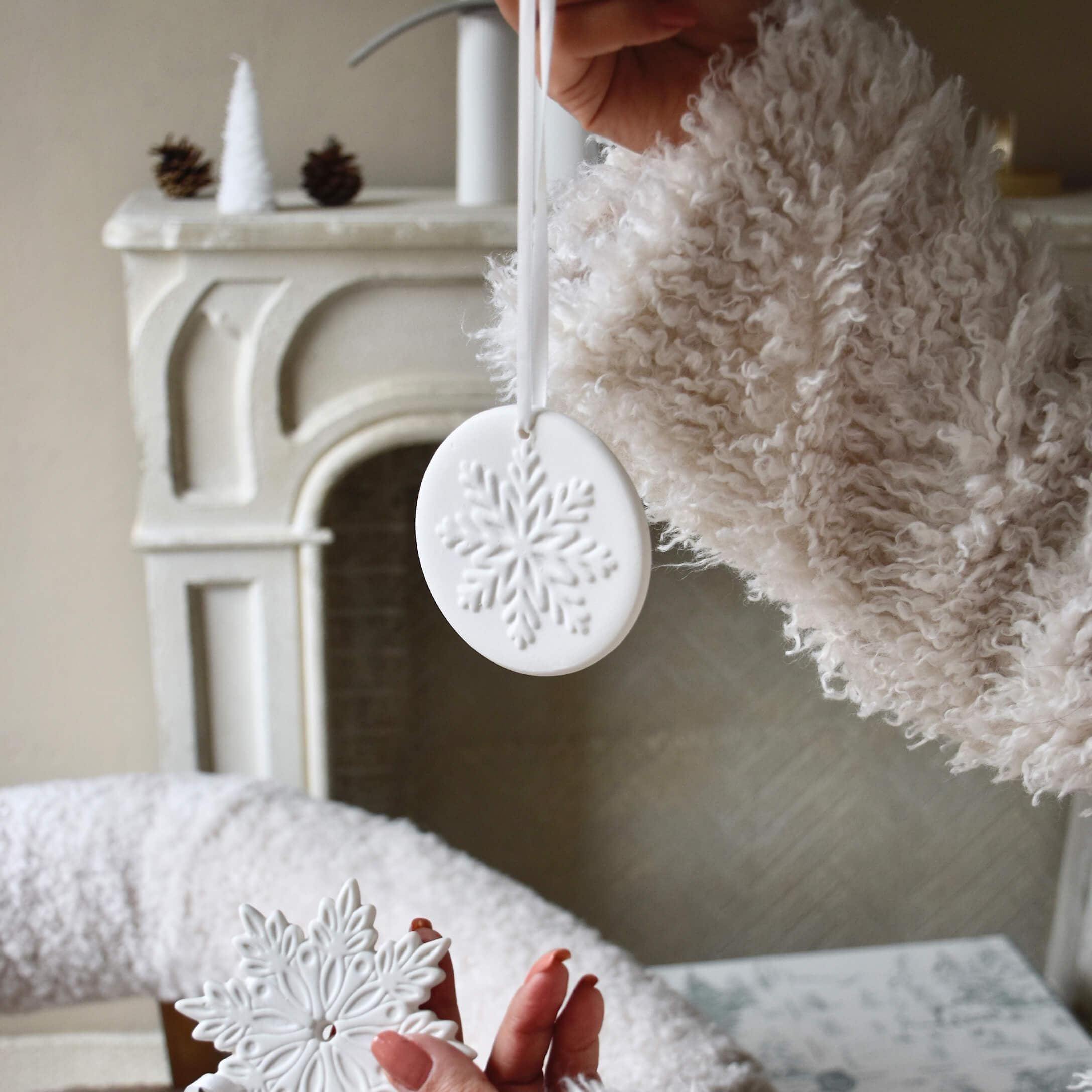 Witte keramische kerstversieringen met sneeuwvlokmotief, vastgehouden voor een open haard en zachte trui