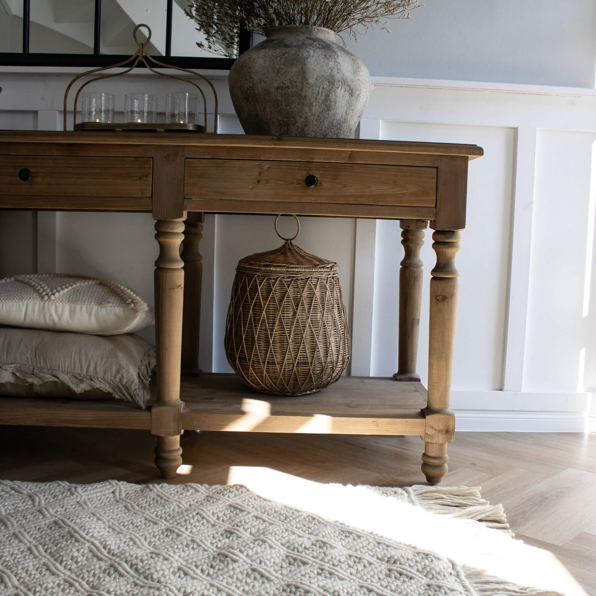 Beige geweven vloerkleed met franjes op lichte houten vloer naast rustieke dennenhouten tafel