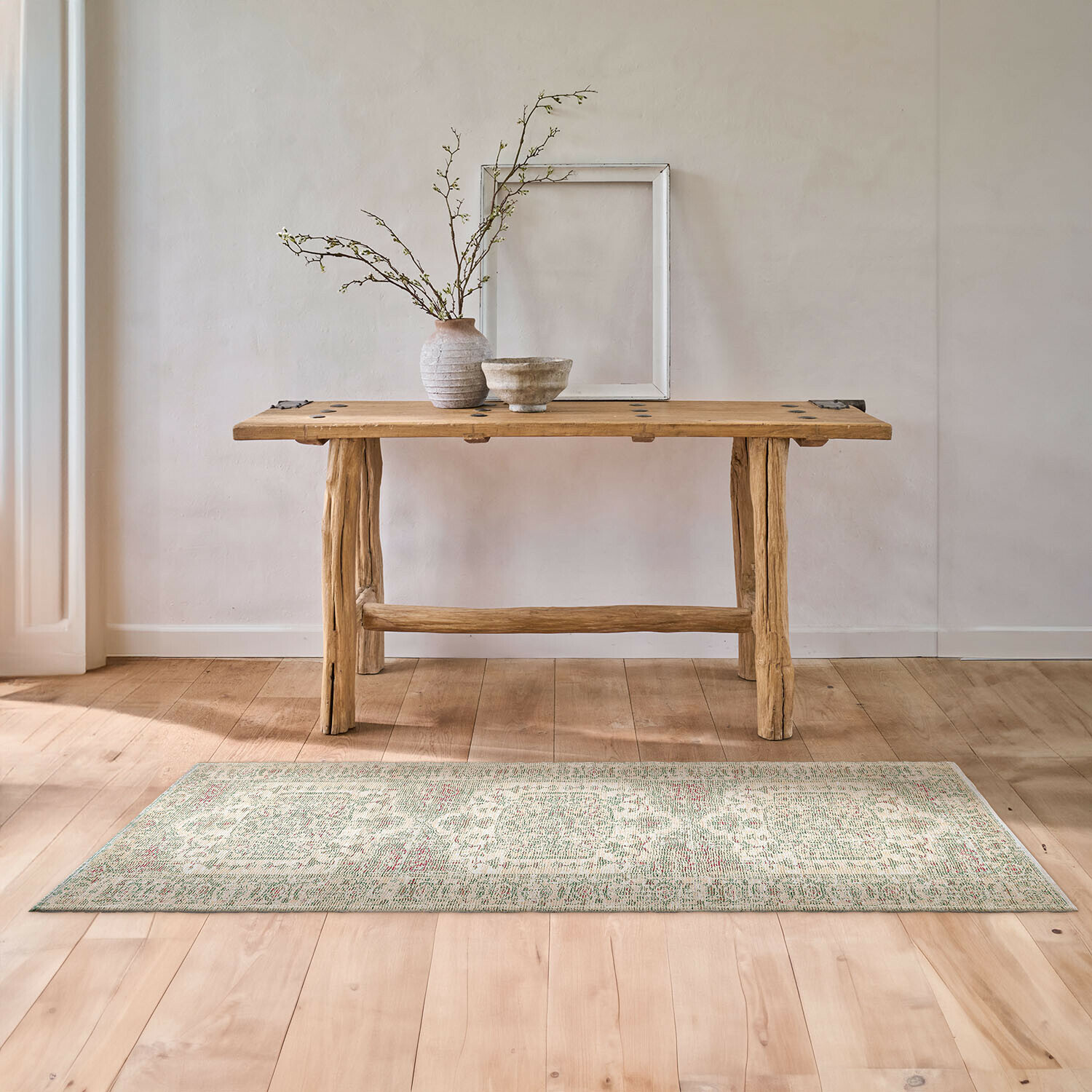 Houten tafel van natuurlijk hout met vaas en kom op lichte vloerkleed in minimalistisch interieur