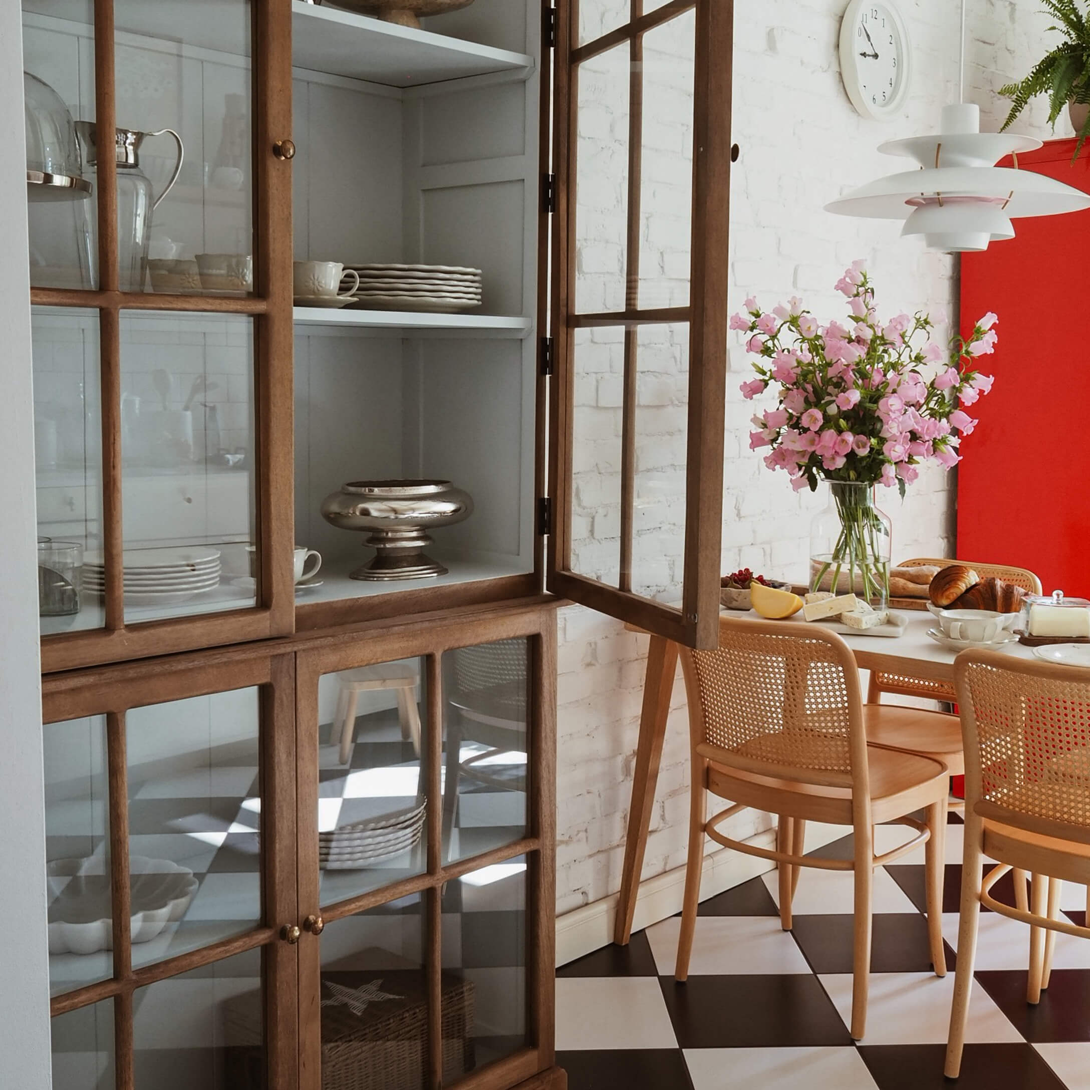 Lichte eetkamer met houten vitrinekast, roze bloemen en zwart-witte dambordvloer