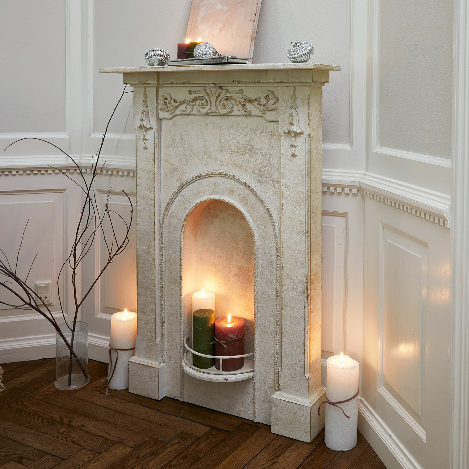 Haardschouw Câlanette Decoratieve witte schoorsteen met sierlijke details en brandende kaarsen in woonkamer met houten vloer