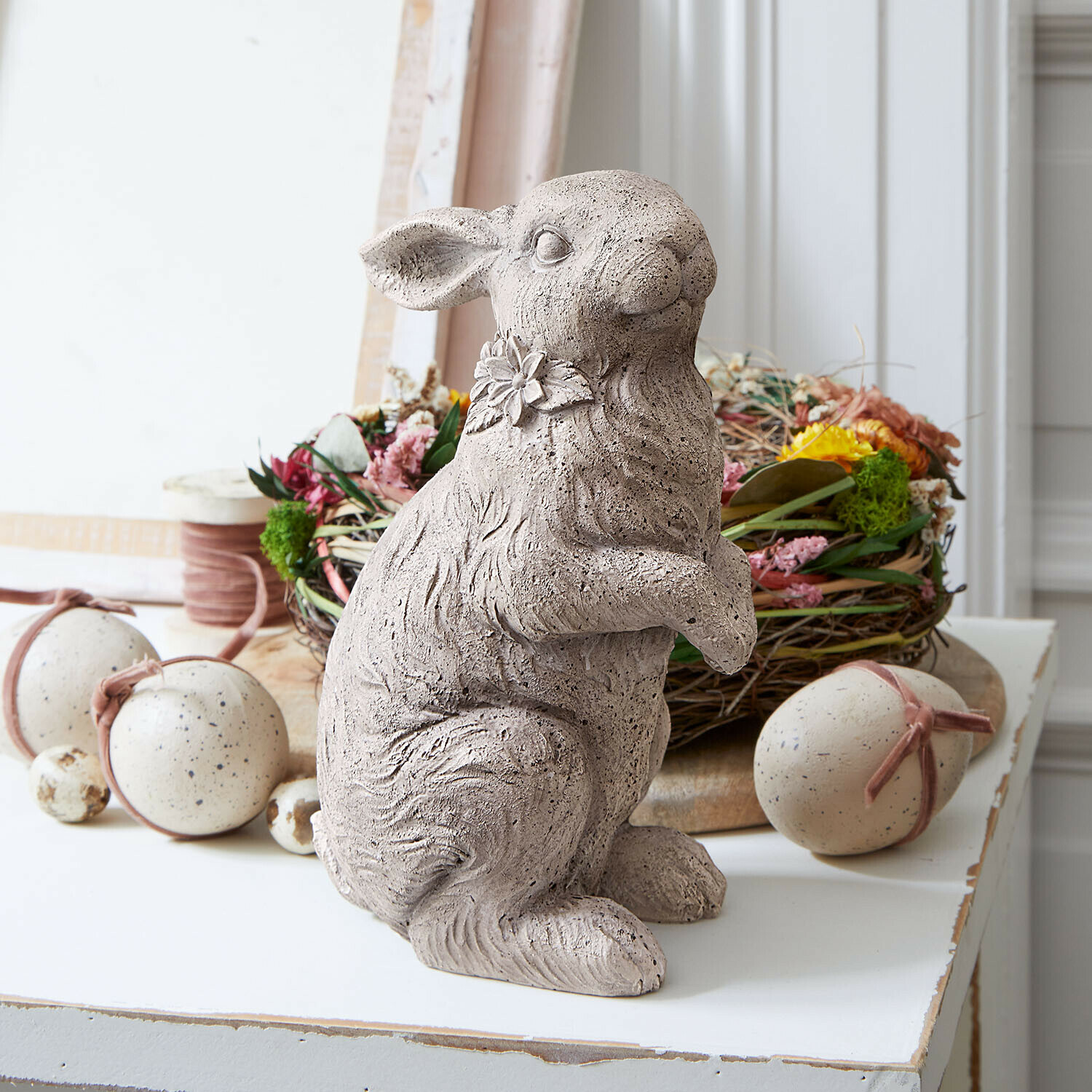 Grijze betonnen konijnenfiguur met bloem aan de nek, paasdecoratie voor op tafel