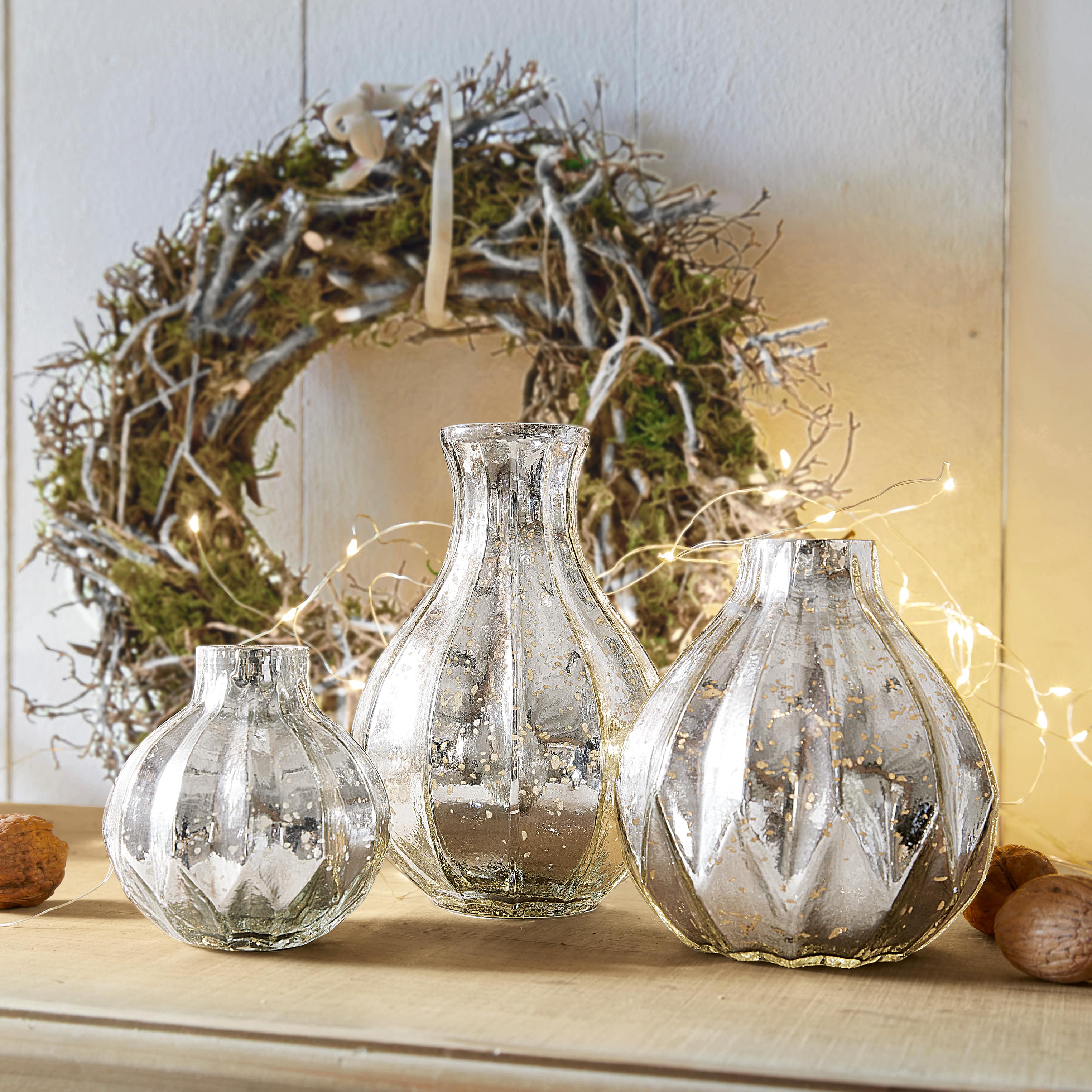 Set van drie decoratieve zilverkleurige glazen vazen met verouderde afwerking op een houten tafel