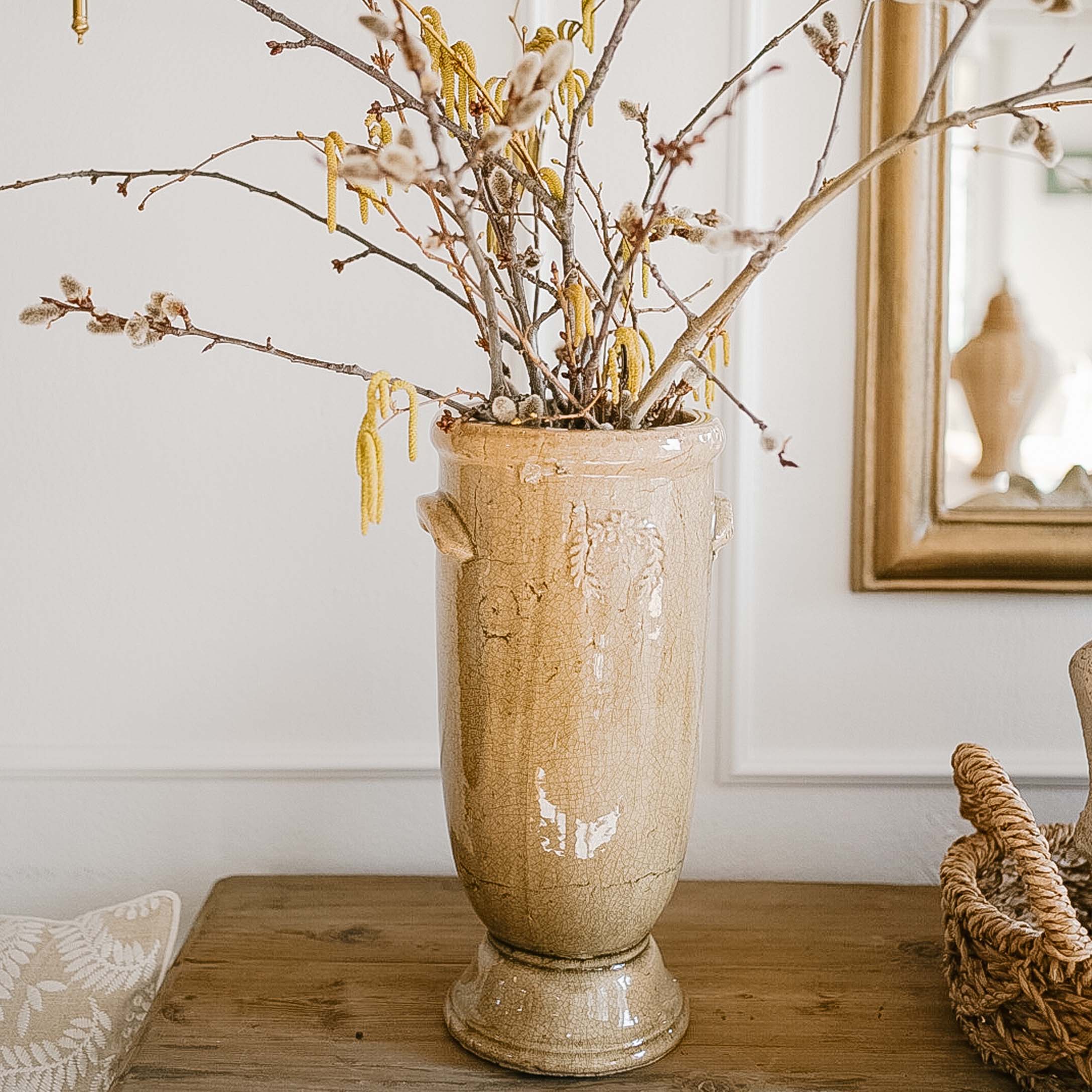 Beige keramische vaas met bloemen en takken op houten tafel in lichte kamer