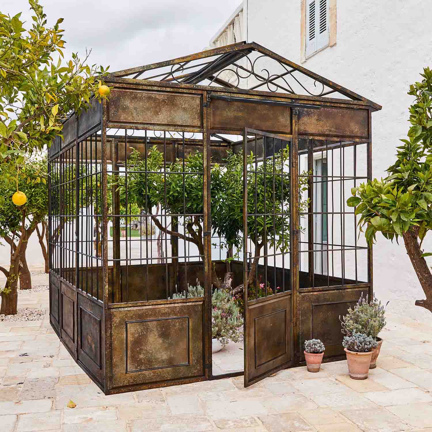 Vintage metalen tuinpaviljoen met planten en citrusbomen op een stenen terras
