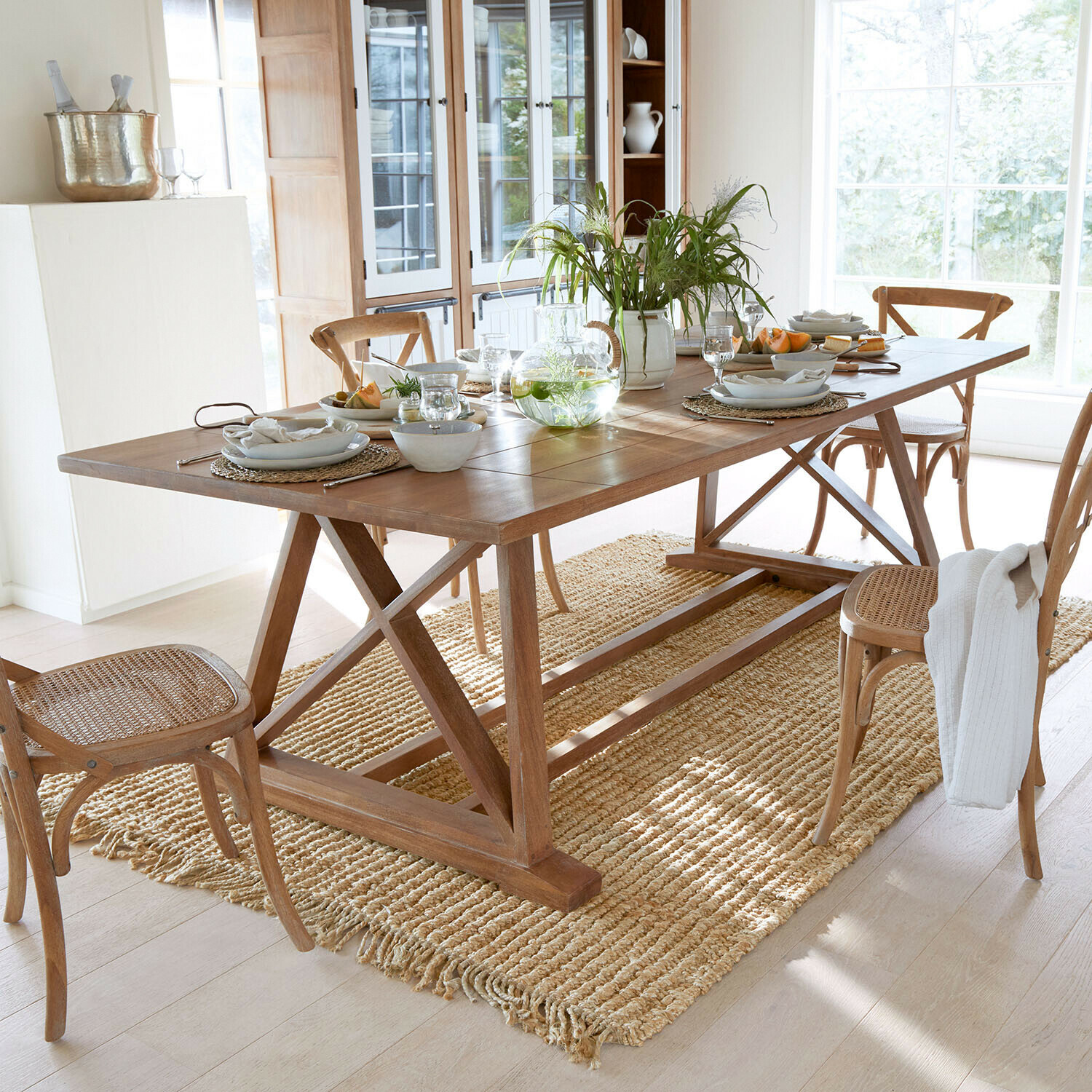 Tafel Isaverny Houten eettafel met stoelen en natuurlijke vloerkleed in lichte kamer met gedekte tafel