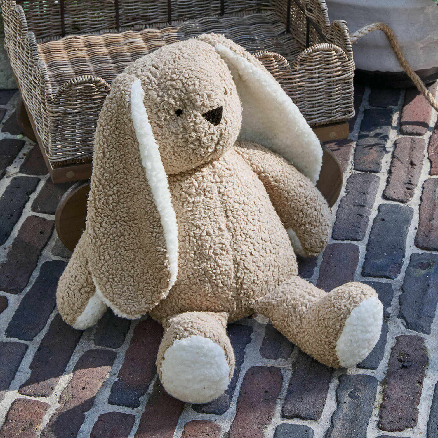 Zachte beige pluchen konijn met witte oren en poten op een bakstenen vloer