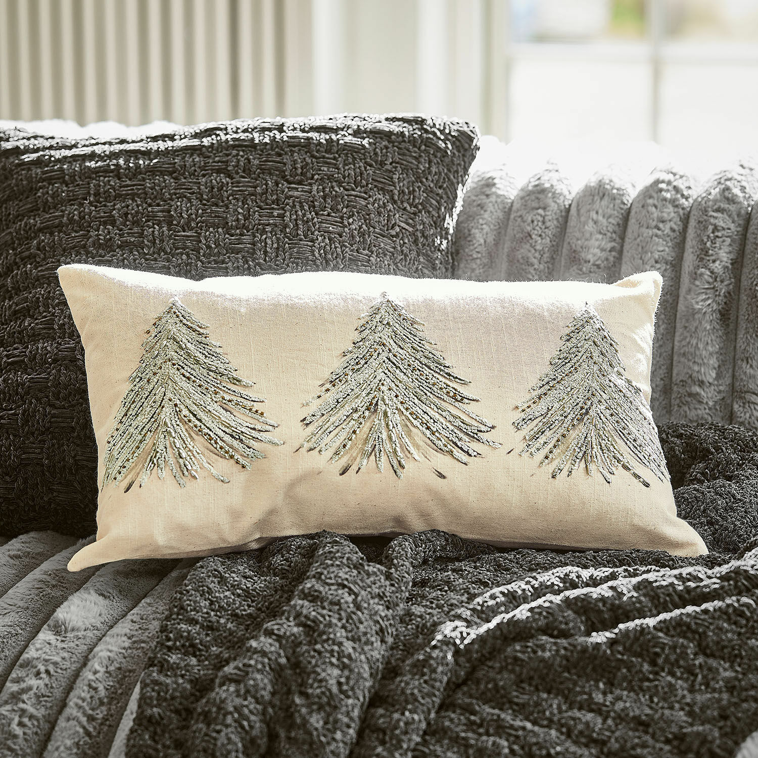 Beige sierkussen met zilveren kerstboom borduursels op donkergrijze deken en bank