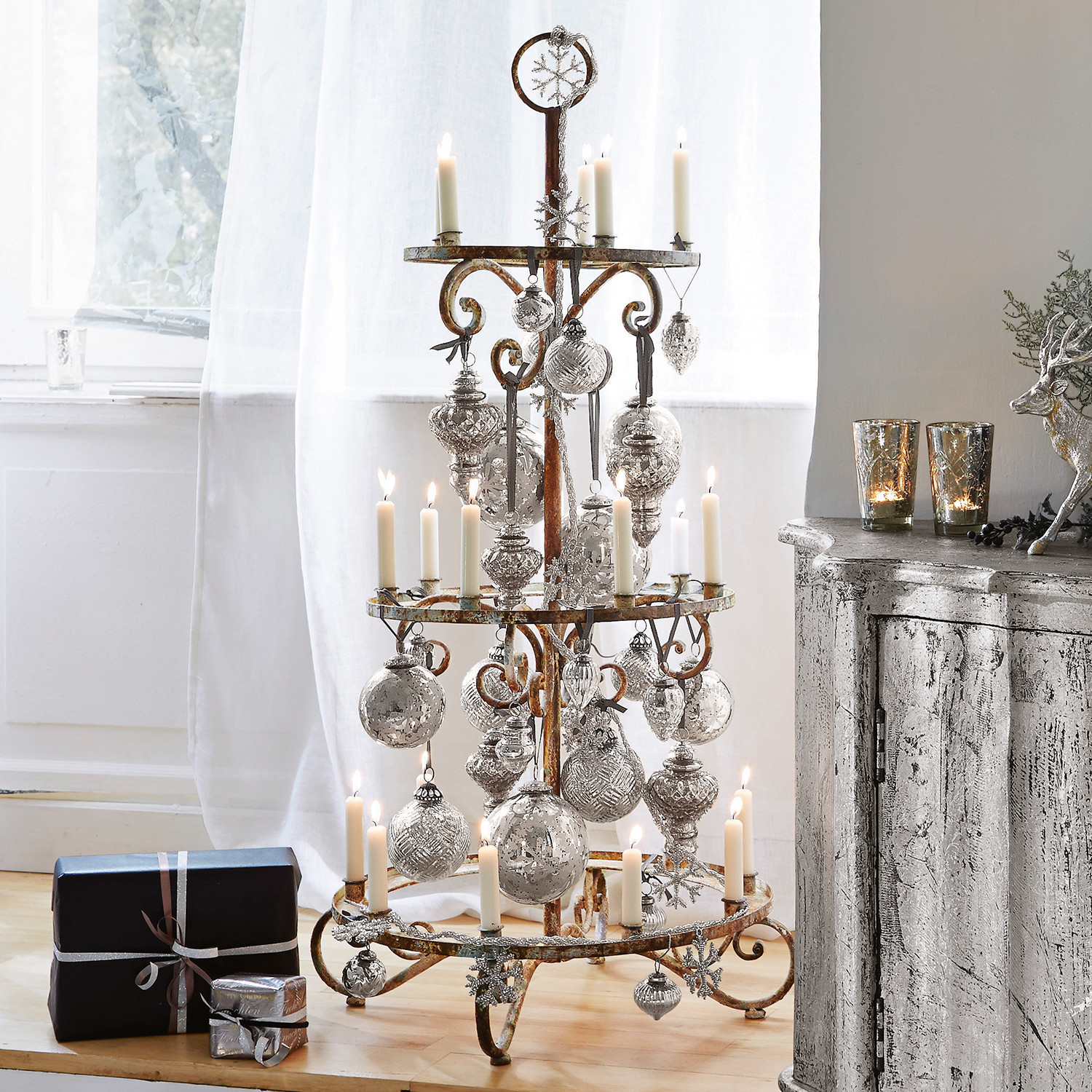 Rustieke metalen kerstdecoratie met witte kaarsen en zilveren ballen op de vloer