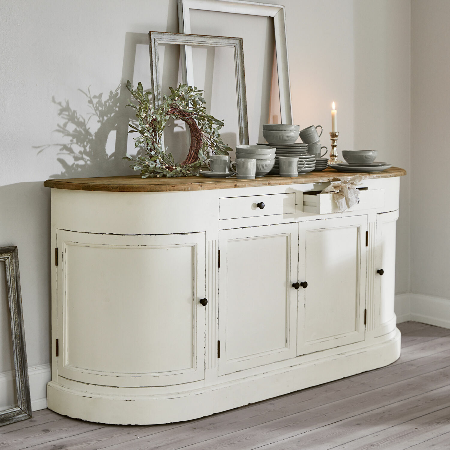 Sideboard Louisiana Witte houten dressoir met houten blad en grijs servies erop, wanddecoraties op de achtergrond