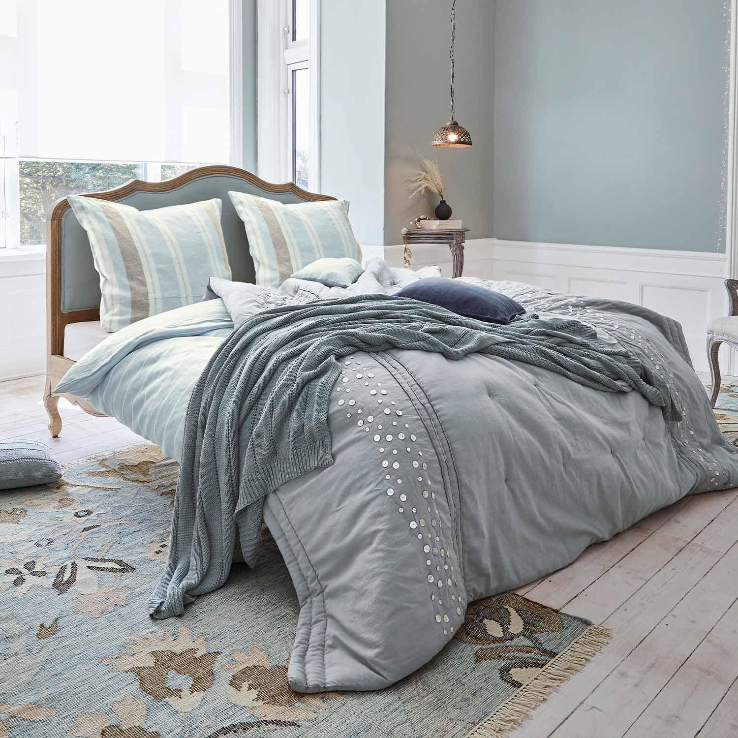 Bed met houten hoofdbord en lichtblauw beddengoed met zachte gebreide deken en kussens