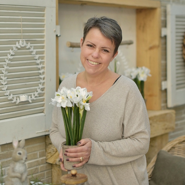 Vrouw houdt pot met witte bloemen vast in natuurlijke paasdecoratie met versieringen