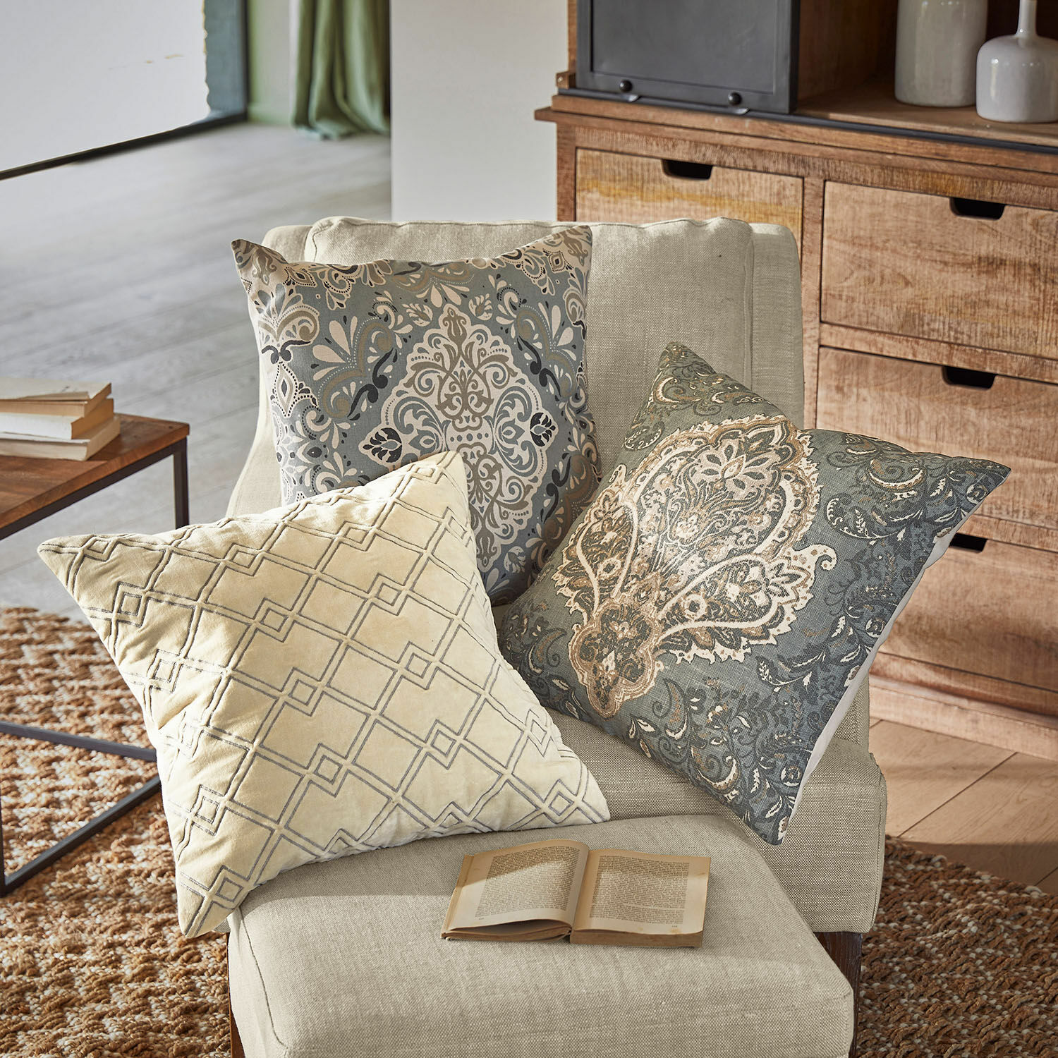 Drie decoratieve kussens met beige en grijze patronen op een lichte fauteuil in de woonkamer