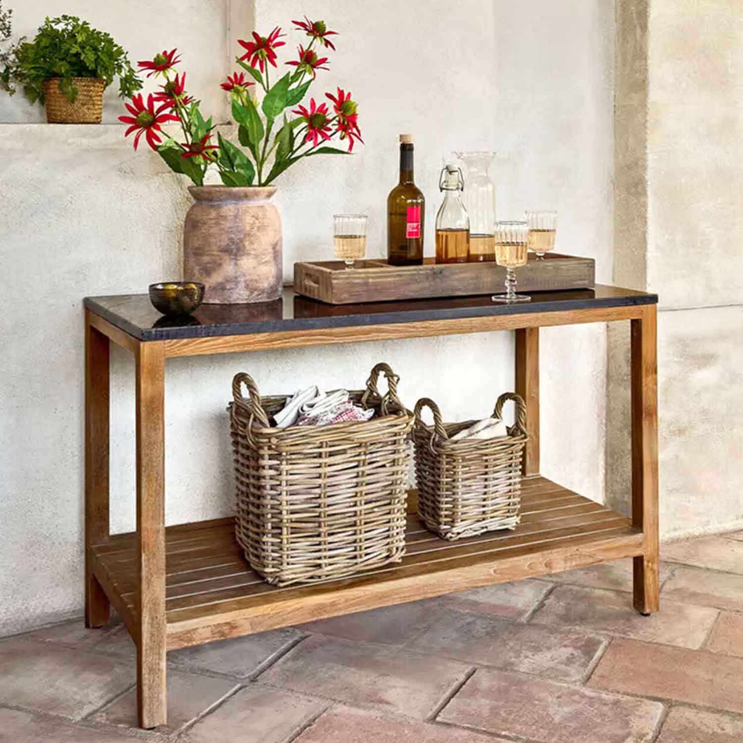 Houten tafel met zwart blad, vaas met rode bloemen en rieten manden eronder in rustieke setting