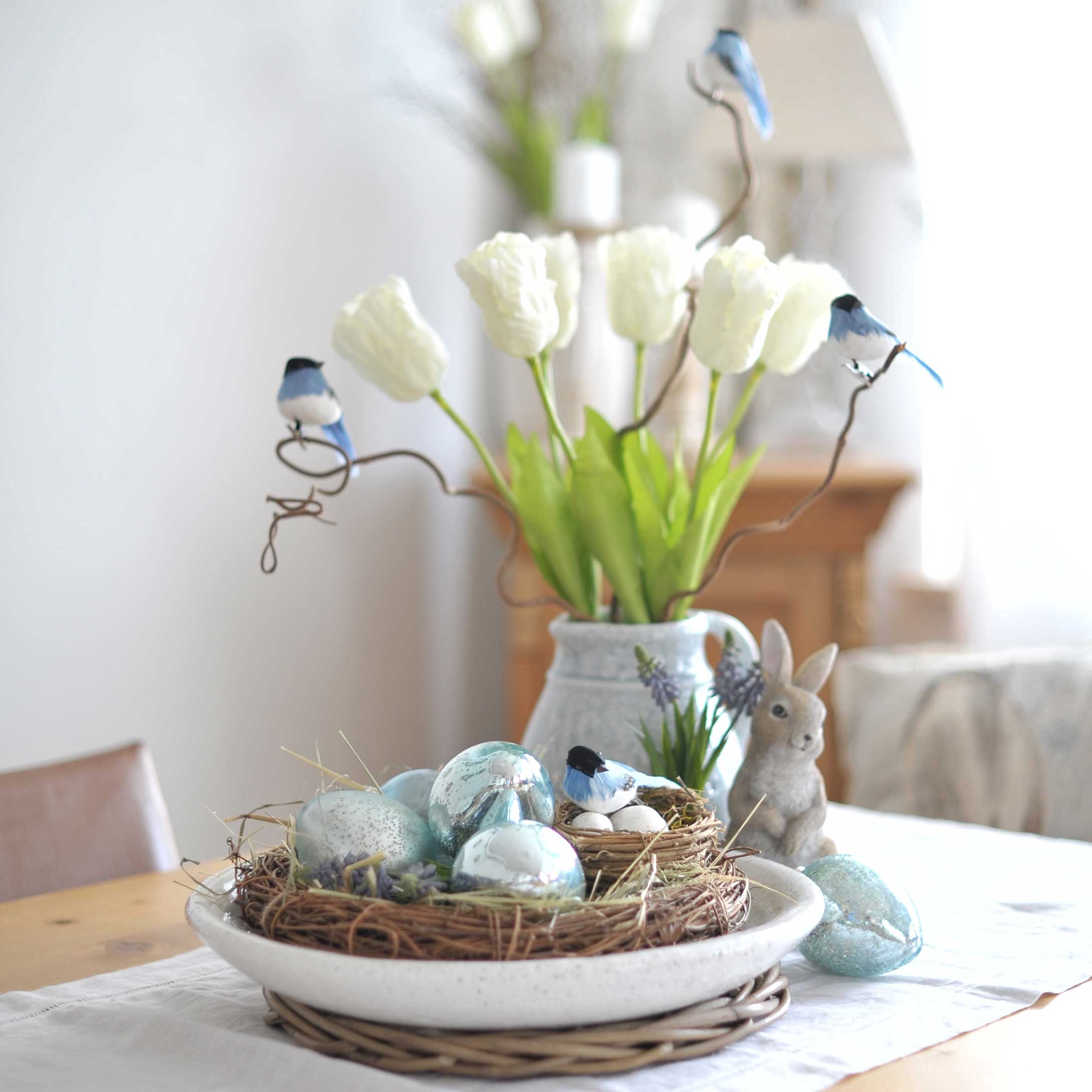 Decoratieve krans met blauwe eieren en vogeltjes op tafel met witte tulpen en konijnenfiguur