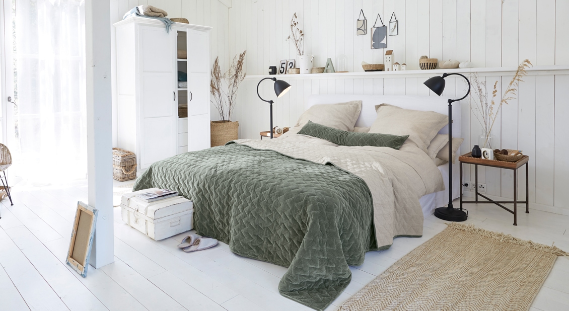 Gezellige slaapkamer met witte kast en bed met groene gewatteerde deken en beige beddengoed