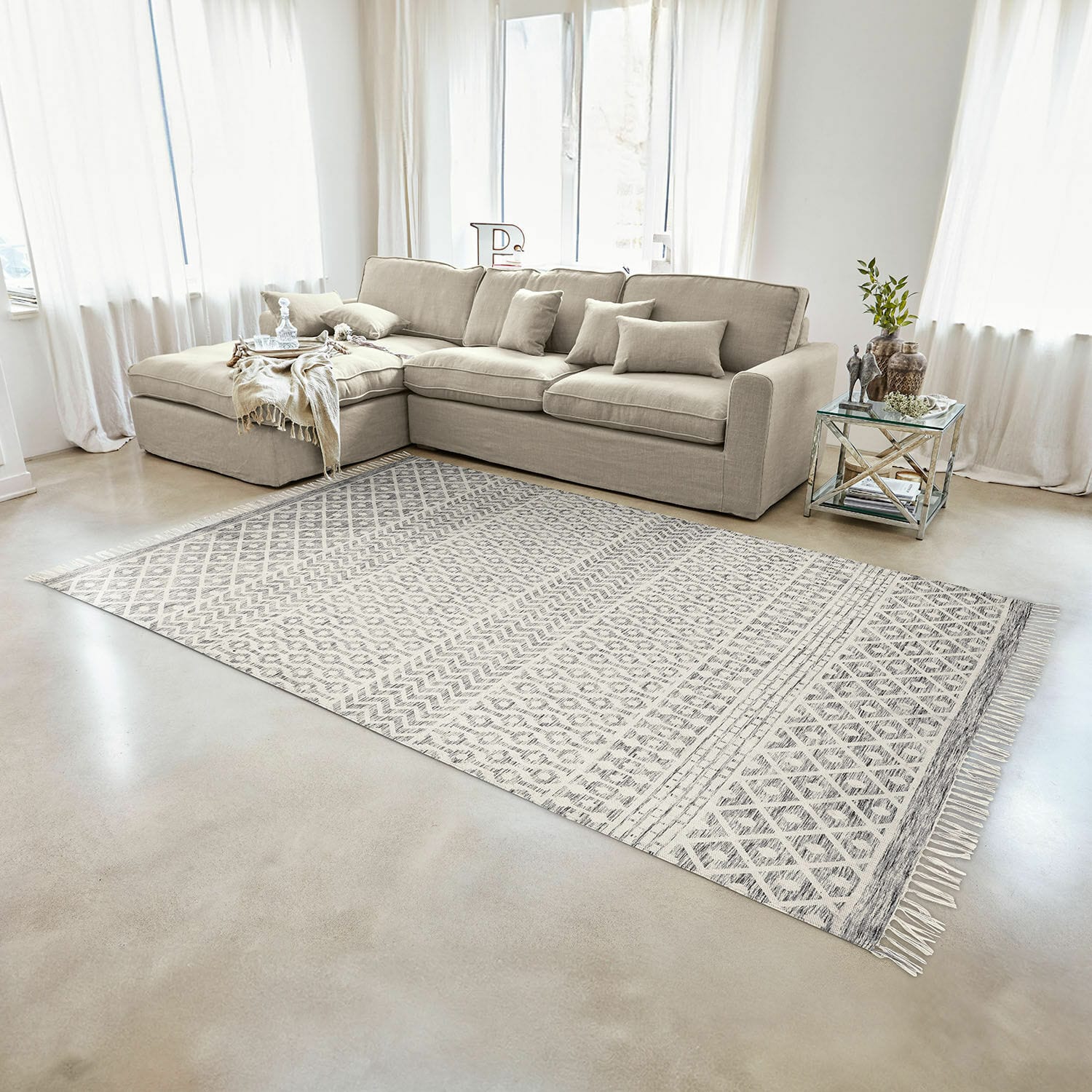 Beige stoffen hoekbank in lichte woonkamer met geometrisch patroon vloerkleed en glazen tafel