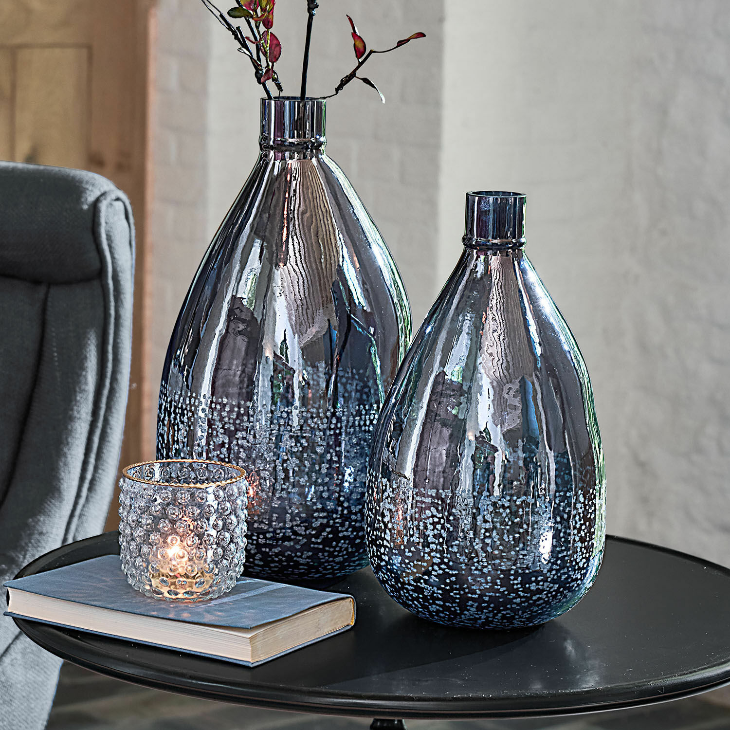 Twee decoratieve rookglas vazen met bubbels patroon op zwarte tafel met boek en windlicht