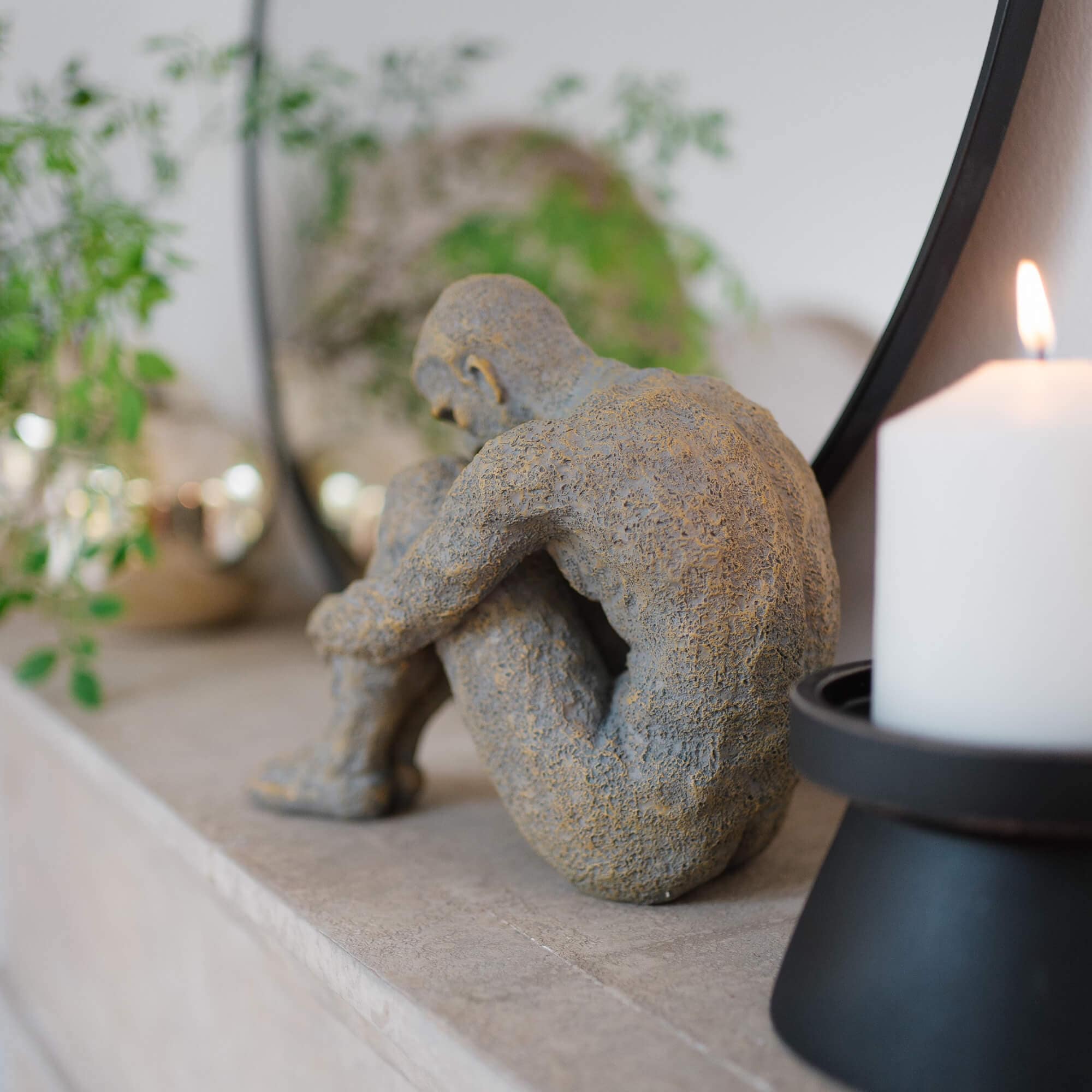 Grijs stenen beeld van zittend figuur op marmeren plank met witte kaars