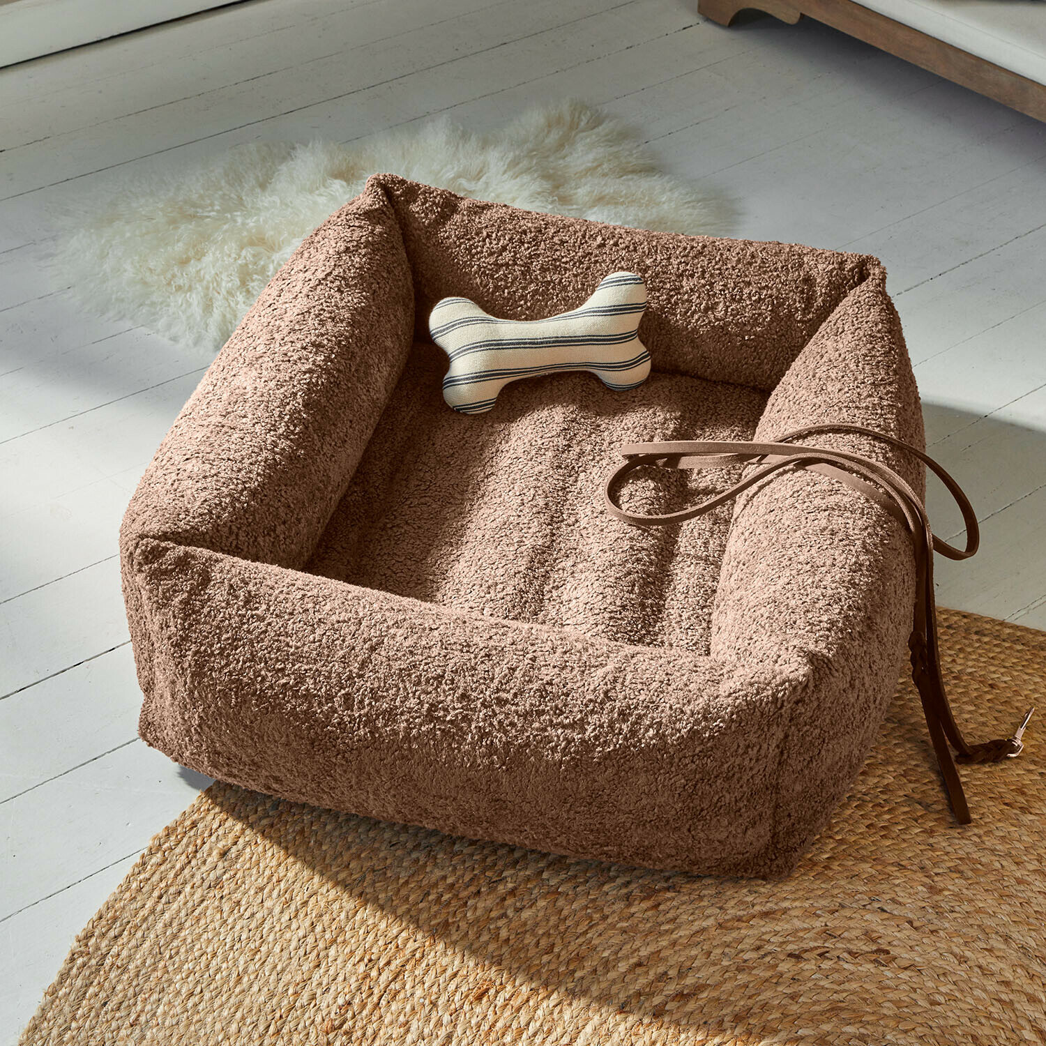 Bruin pluche hondenmand met botvormig kussen en leren riem op gevlochten vloerkleed