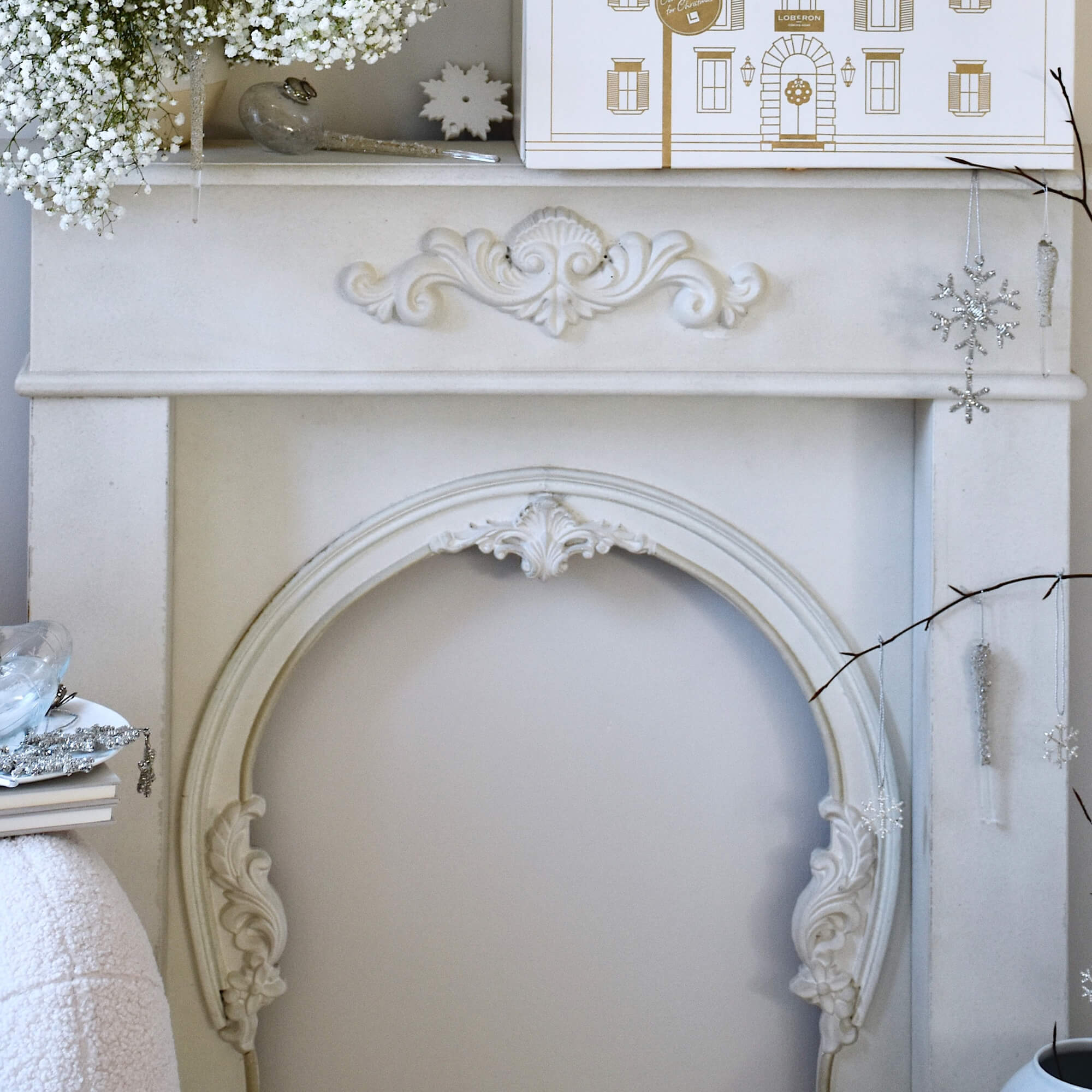 Witte schoorsteenconsole met decoratieve houtsnijwerk en hangende kerstversieringen