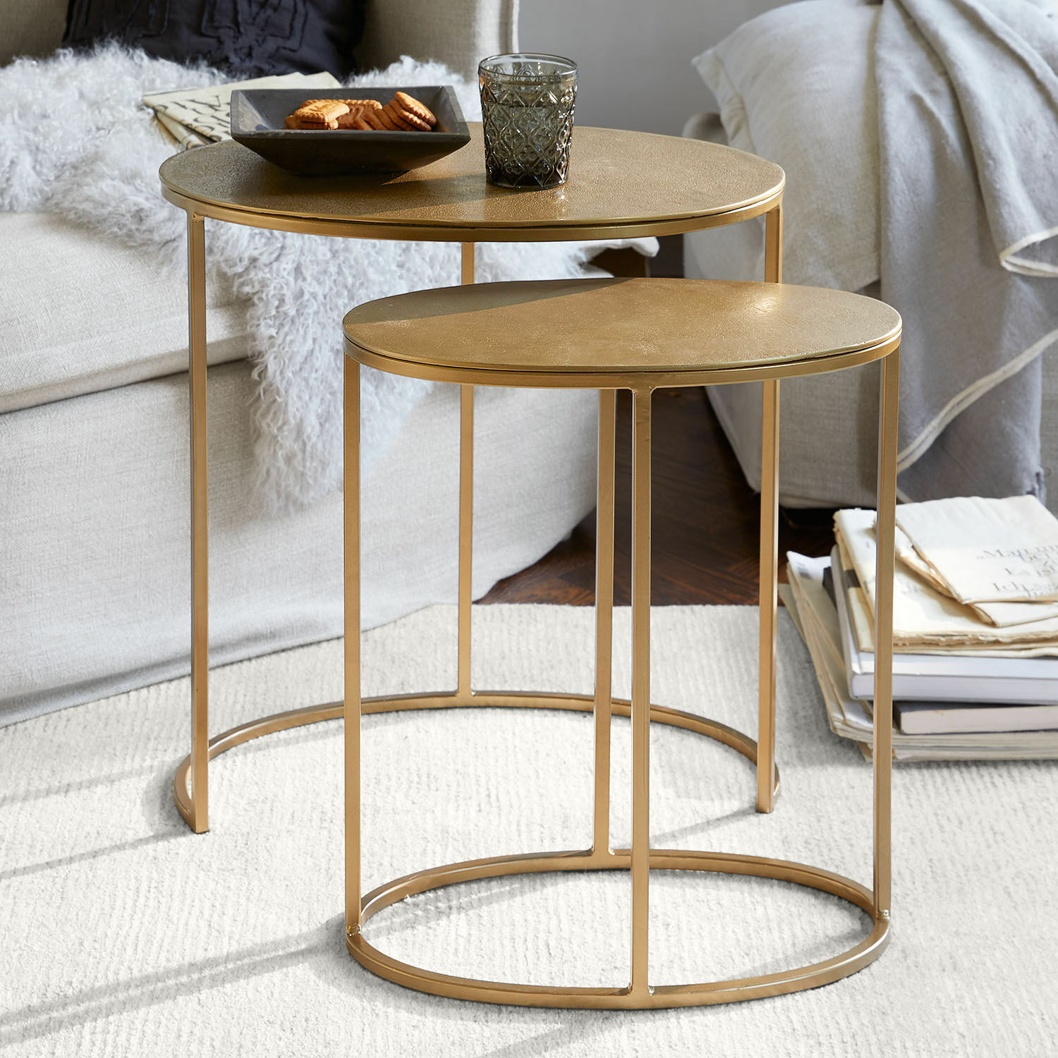 Set van twee gouden metalen ronde bijzettafels op lichte vloerbedekking in woonkamer