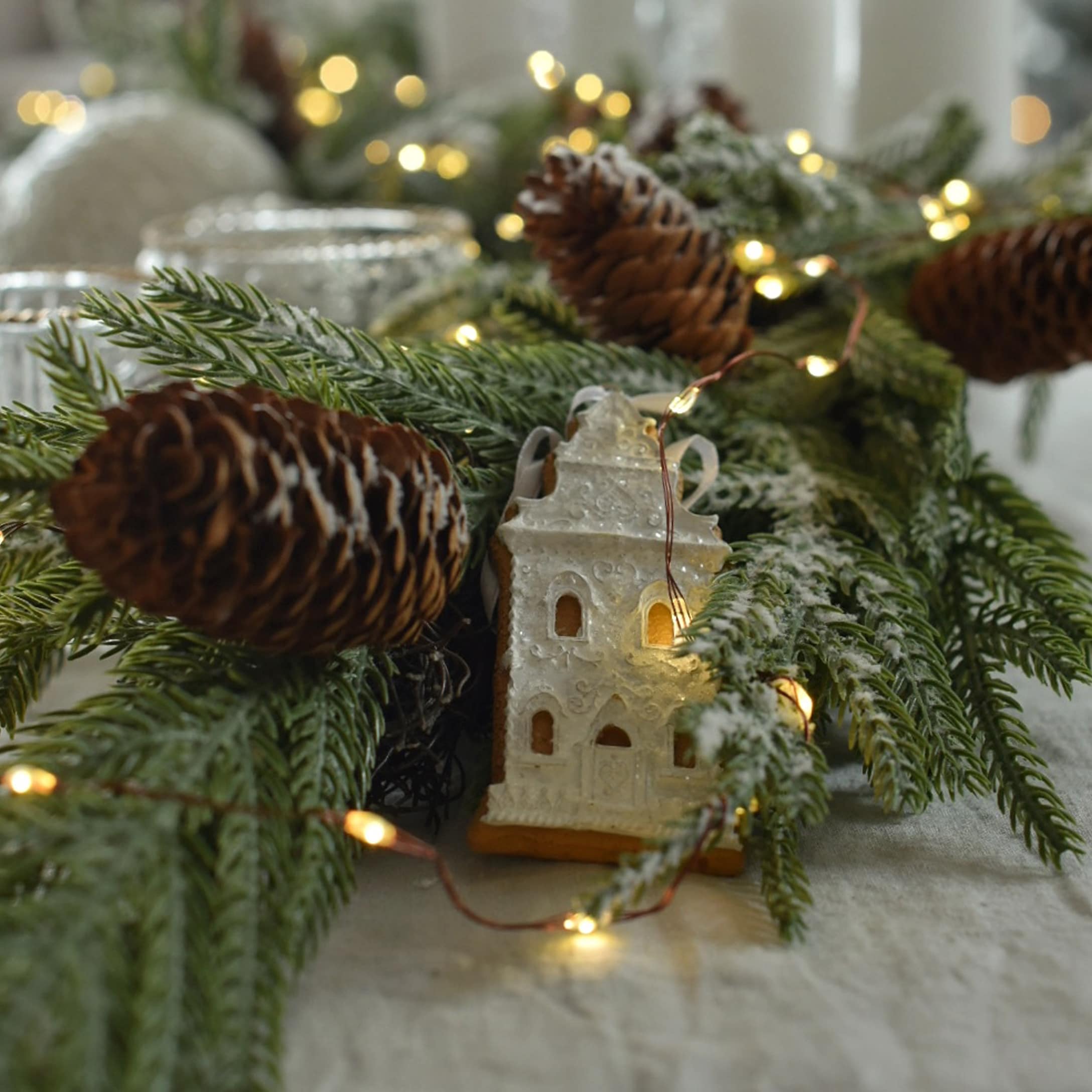 Kerstdecoratie met groene takken, dennenappels en verlicht peperkoekhuisje op tafel