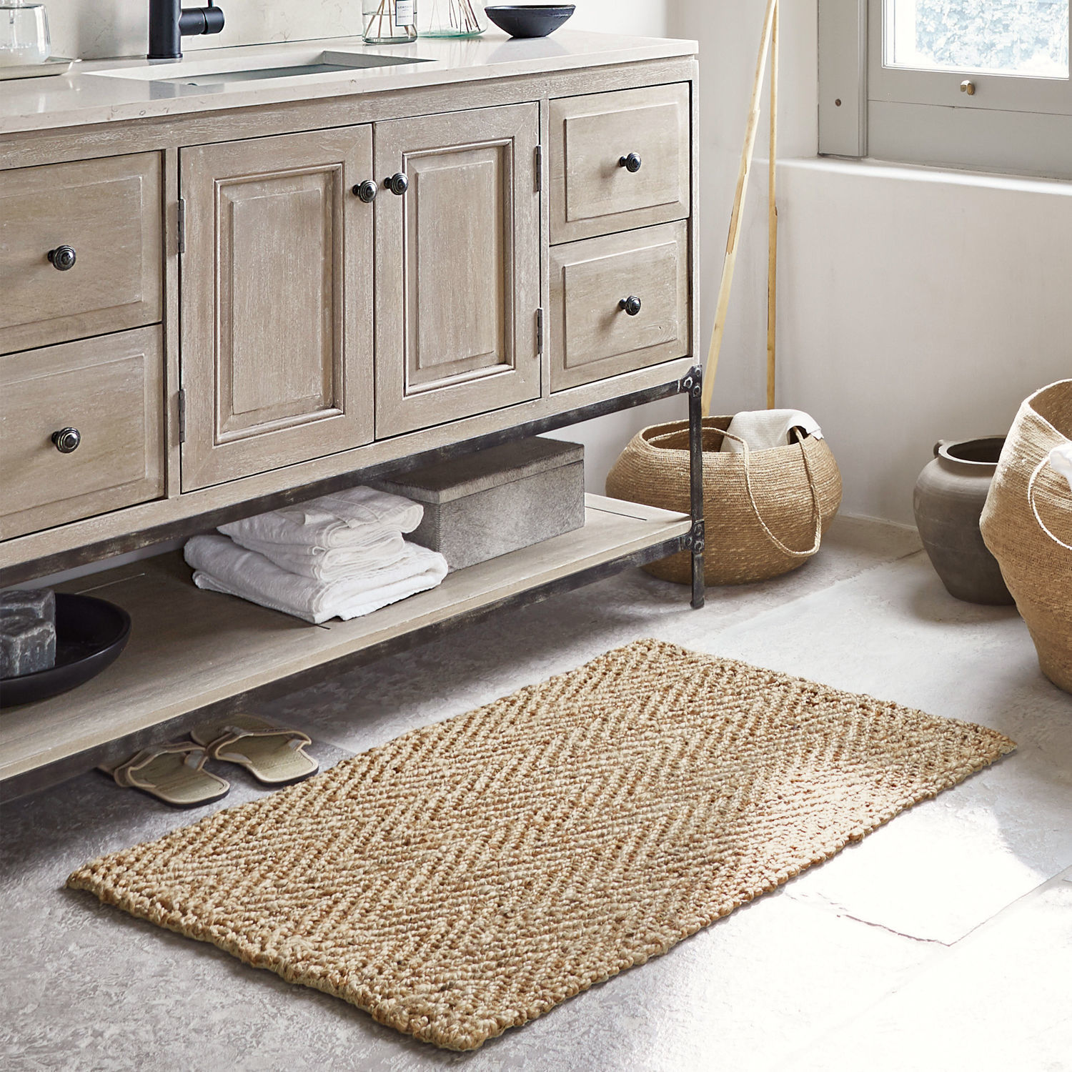 Badmat Daoukro Beige jute vloerkleed met visgraatpatroon in badkamer met houten kast en manden